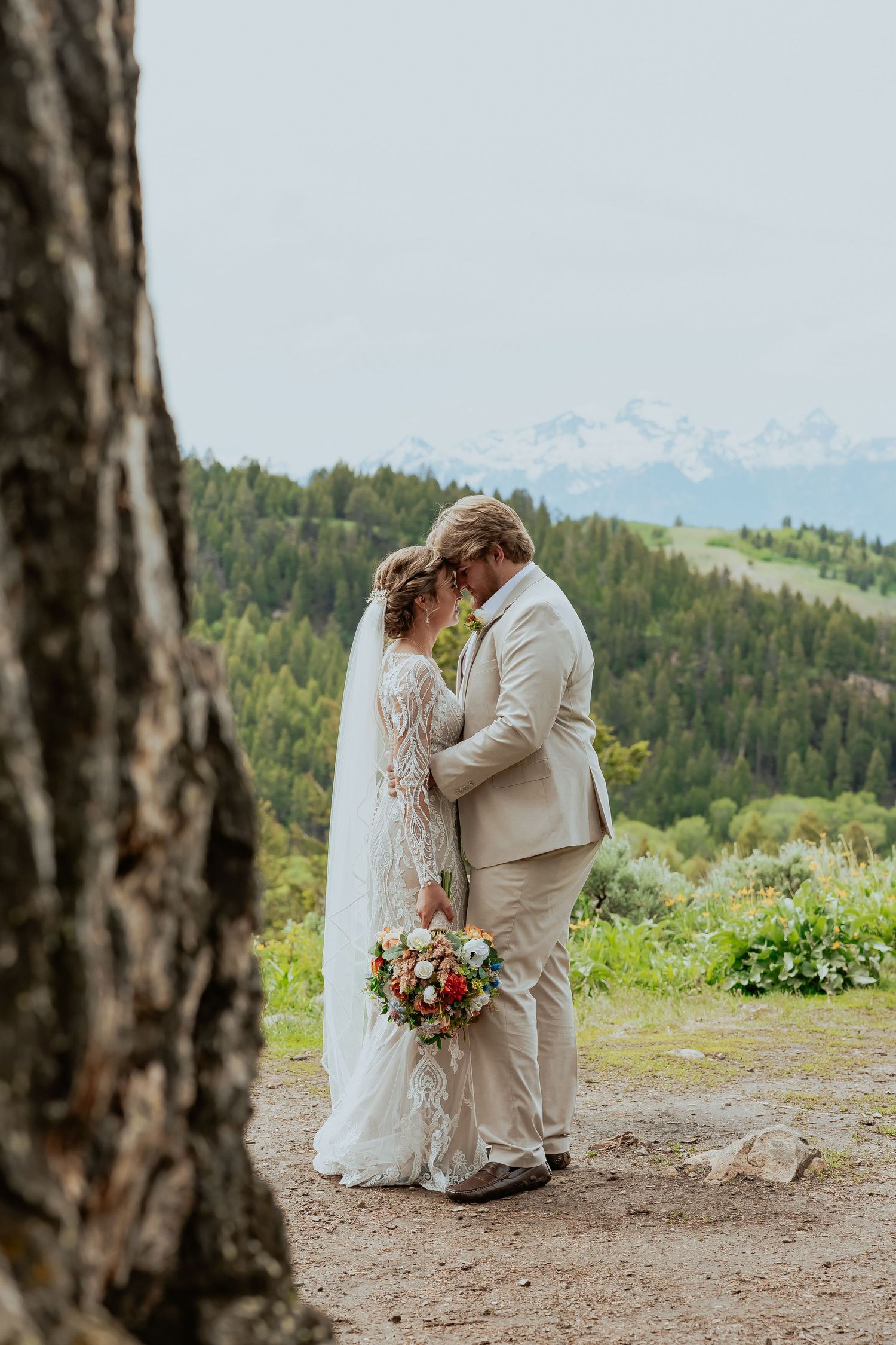 A romantic wedding moment captured on a mountaintop with rolling hills and forests in the background.