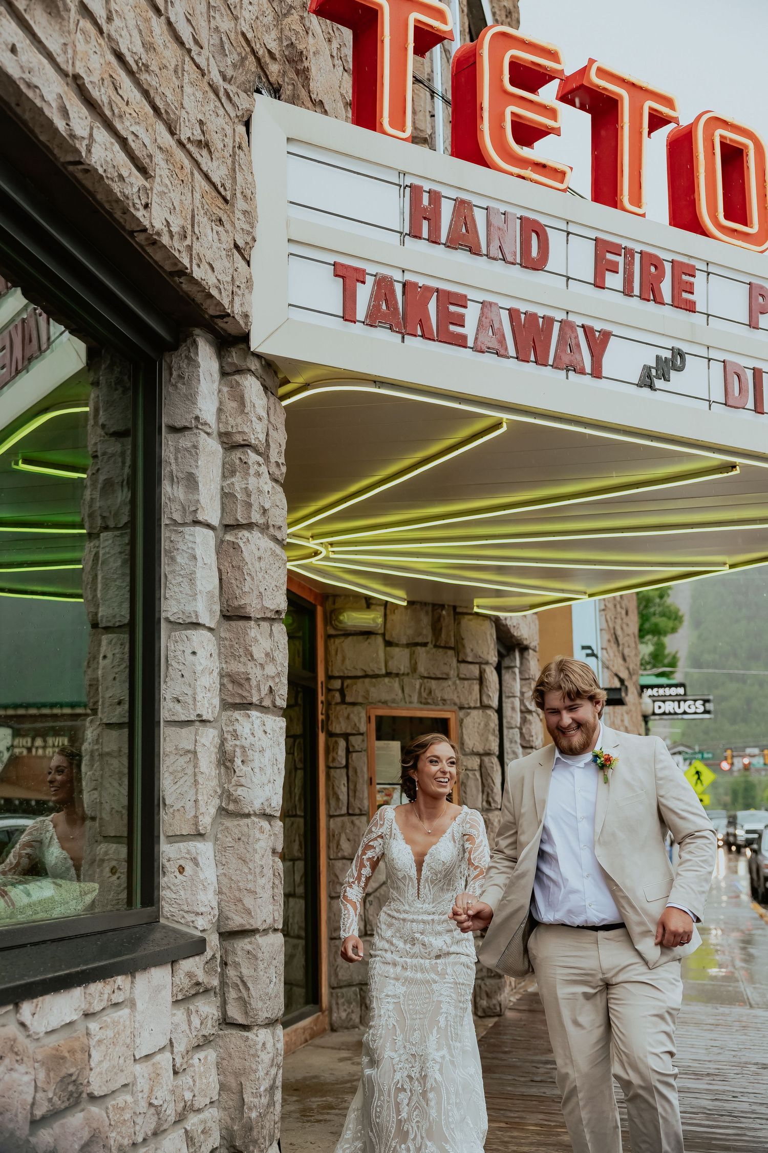 Couple in wedding attire posing outside a retro storefront with neon signage.
