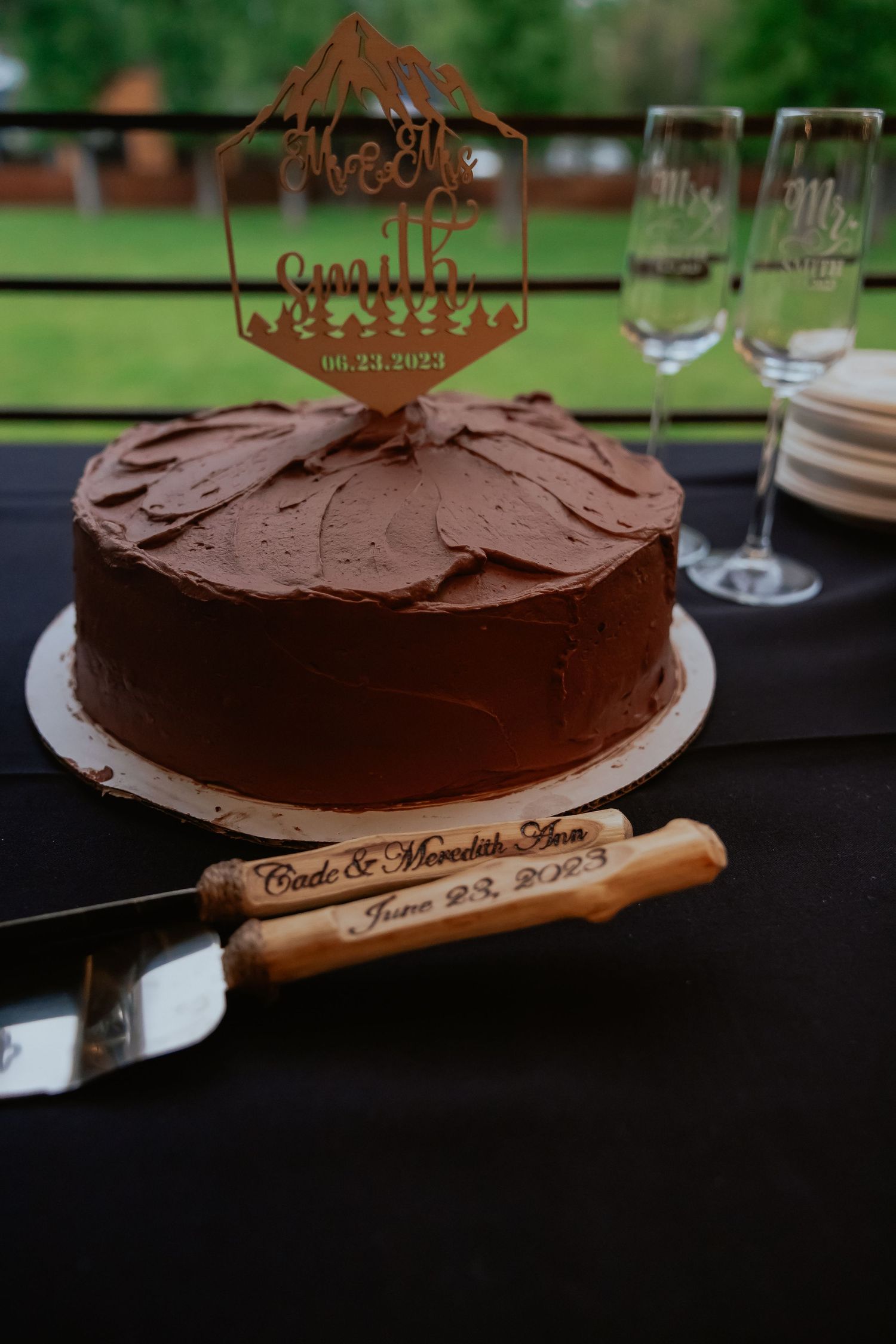 Chocolate frosted cake with wooden serving utensil displayed on dark surface at wedding reception.