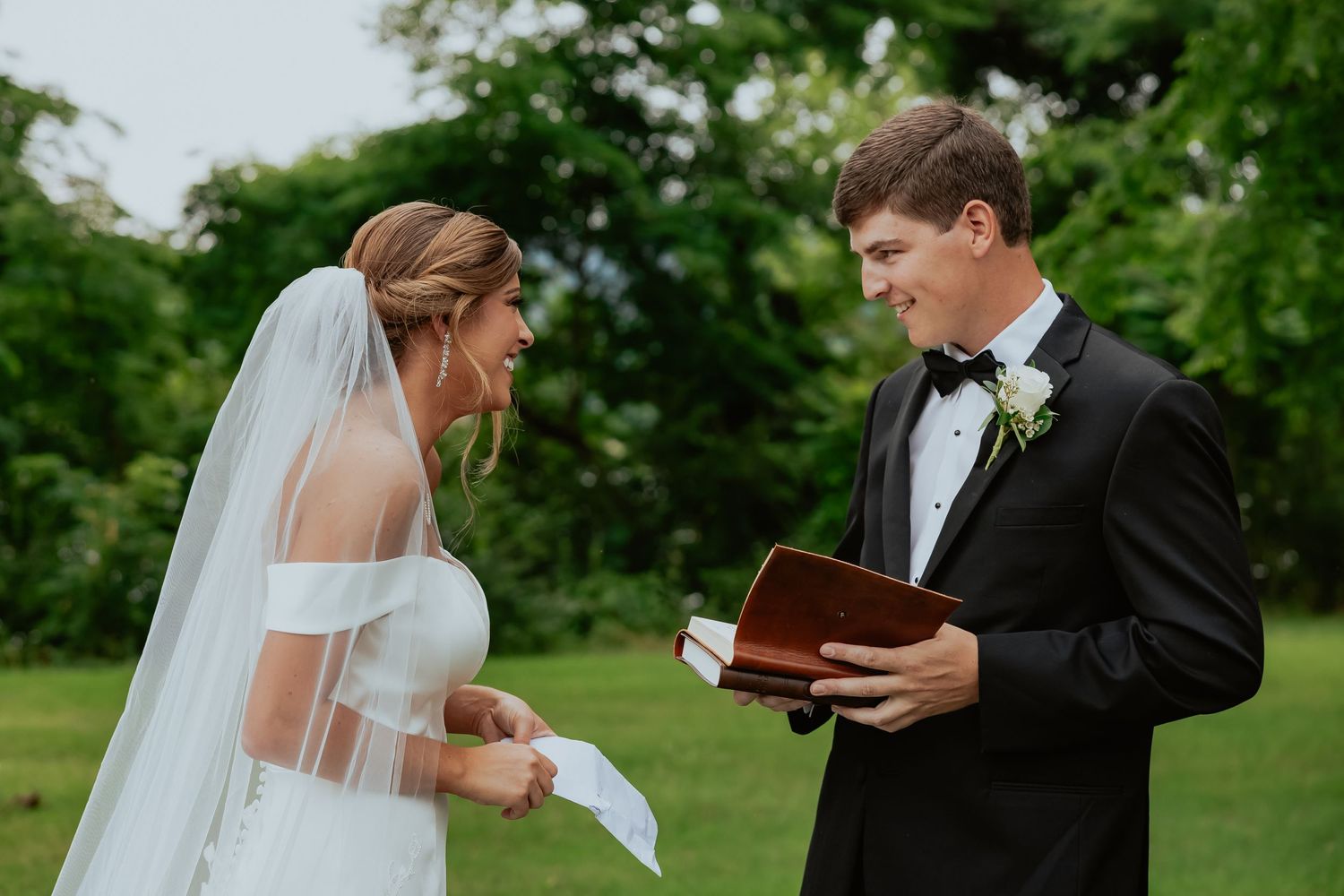 Couple exchanging vows and reading from books during outdoor wedding ceremony.