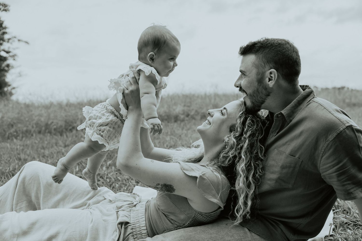 Couple laying in grass sharing playful romantic moments in black and white.