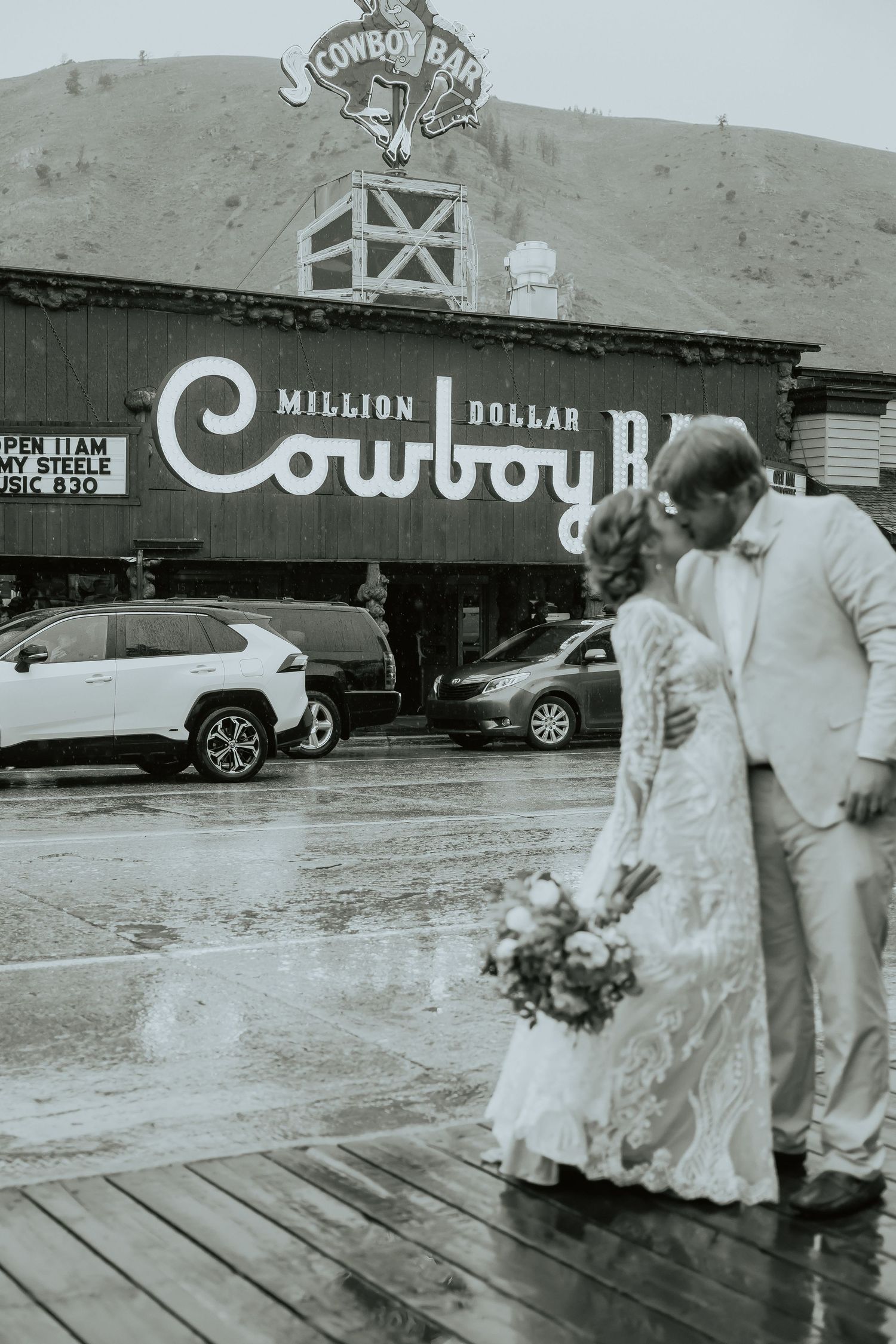 A couple stands outside the iconic Cowboy Bar sign on a rainy day.