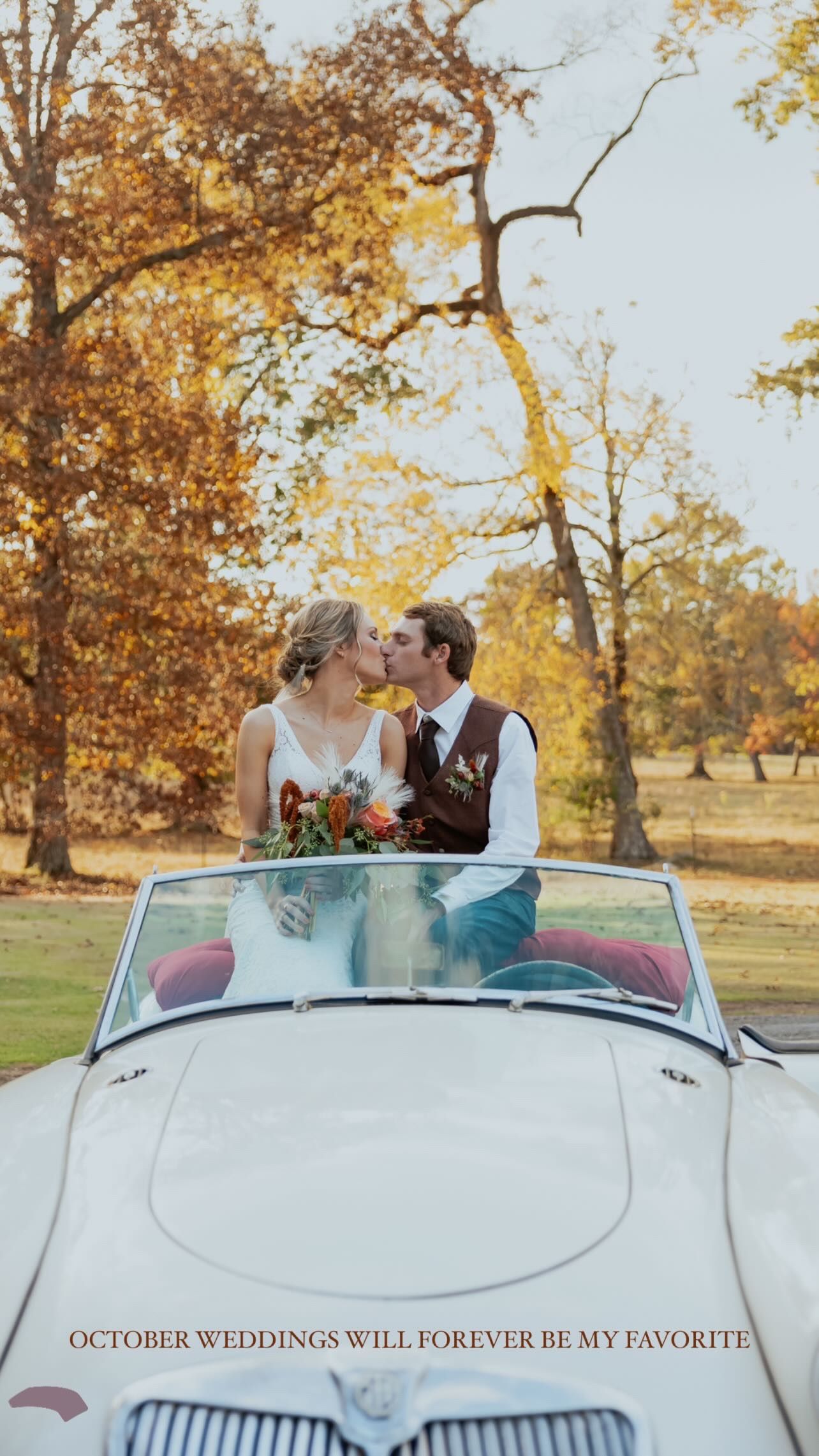 Newlyweds sharing a romantic kiss in a vintage white convertible car during fall.