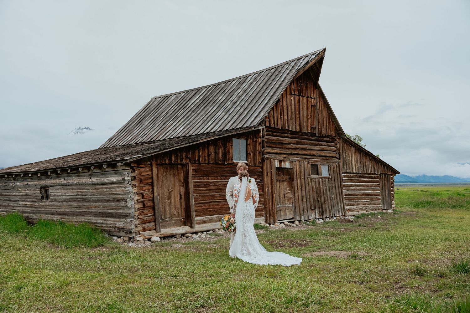 Rustic wooden barns and structures stand against a cloudy sky in an open field.