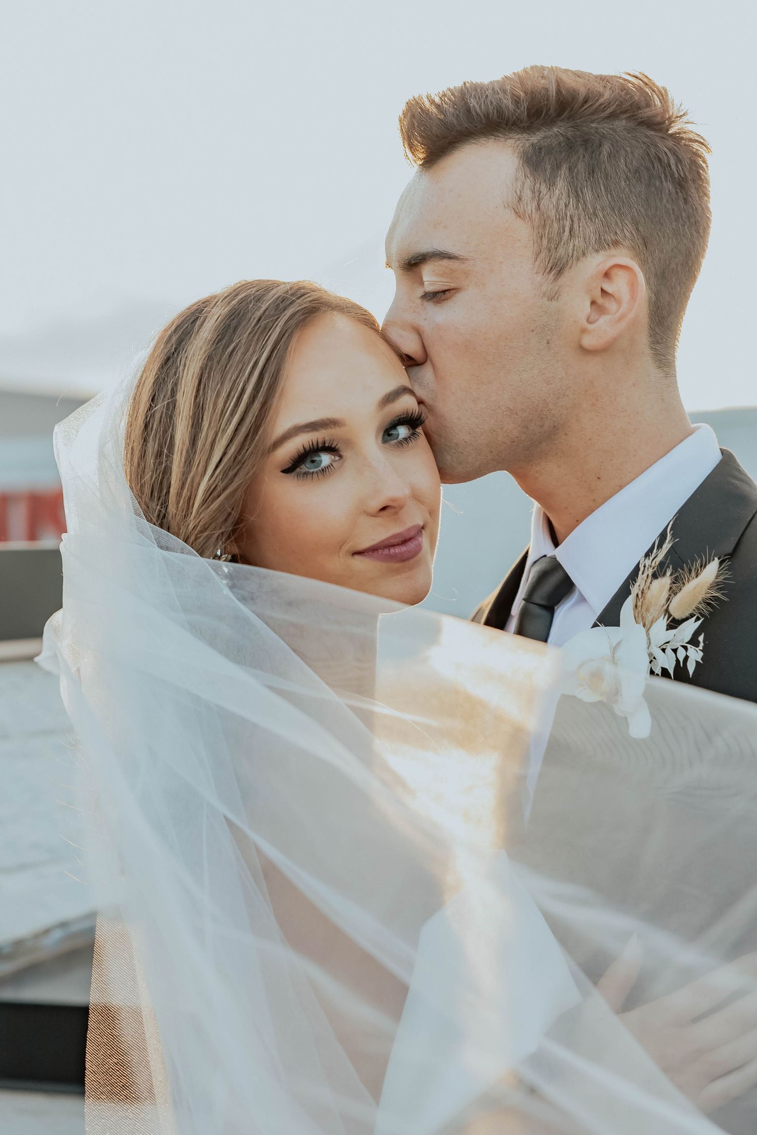 Romantic wedding portrait with flowing veil and intimate kiss.