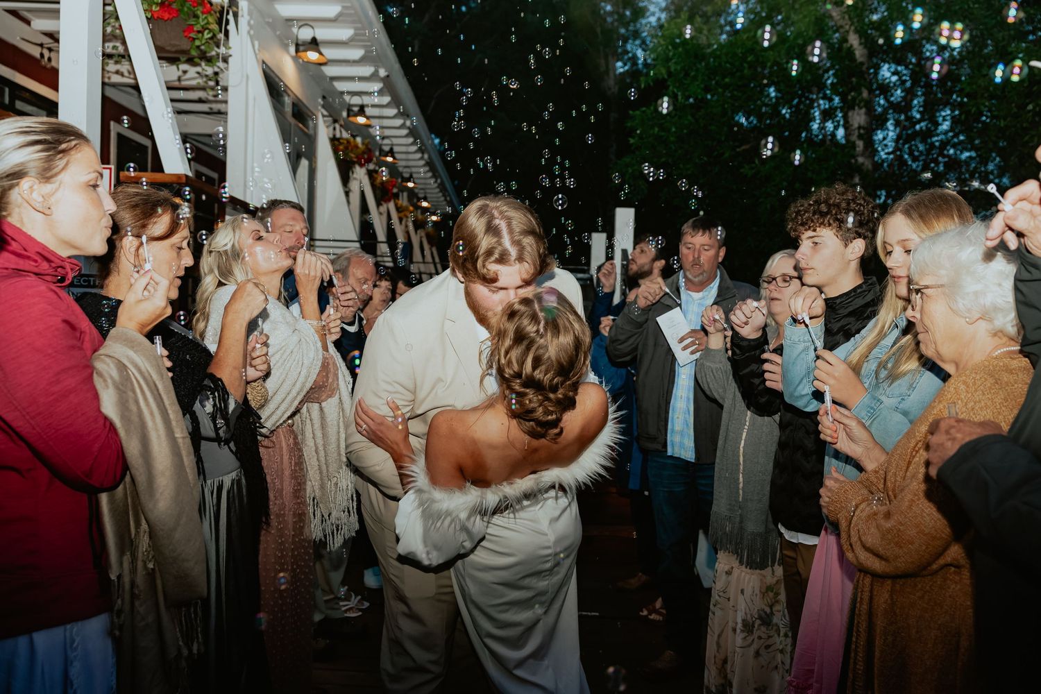 Wedding guests dancing and celebrating under string lights at an outdoor reception.