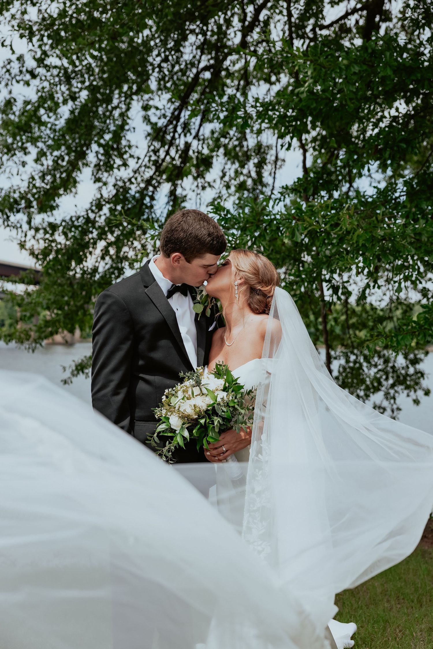 Bride's veil flows dramatically in the wind during outdoor wedding portraits.