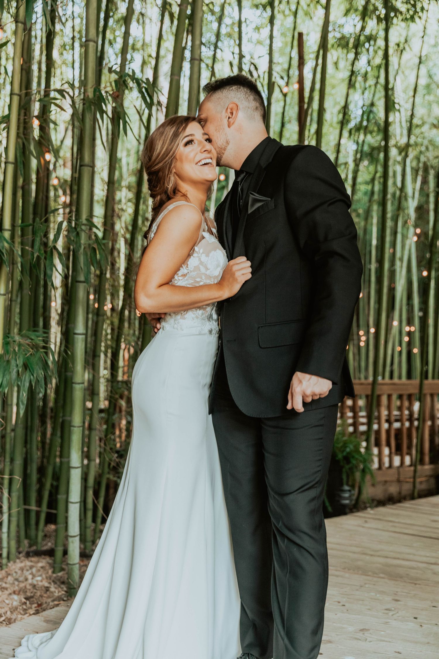 Couple shares intimate moments on wooden walkway surrounded by bamboo forest.