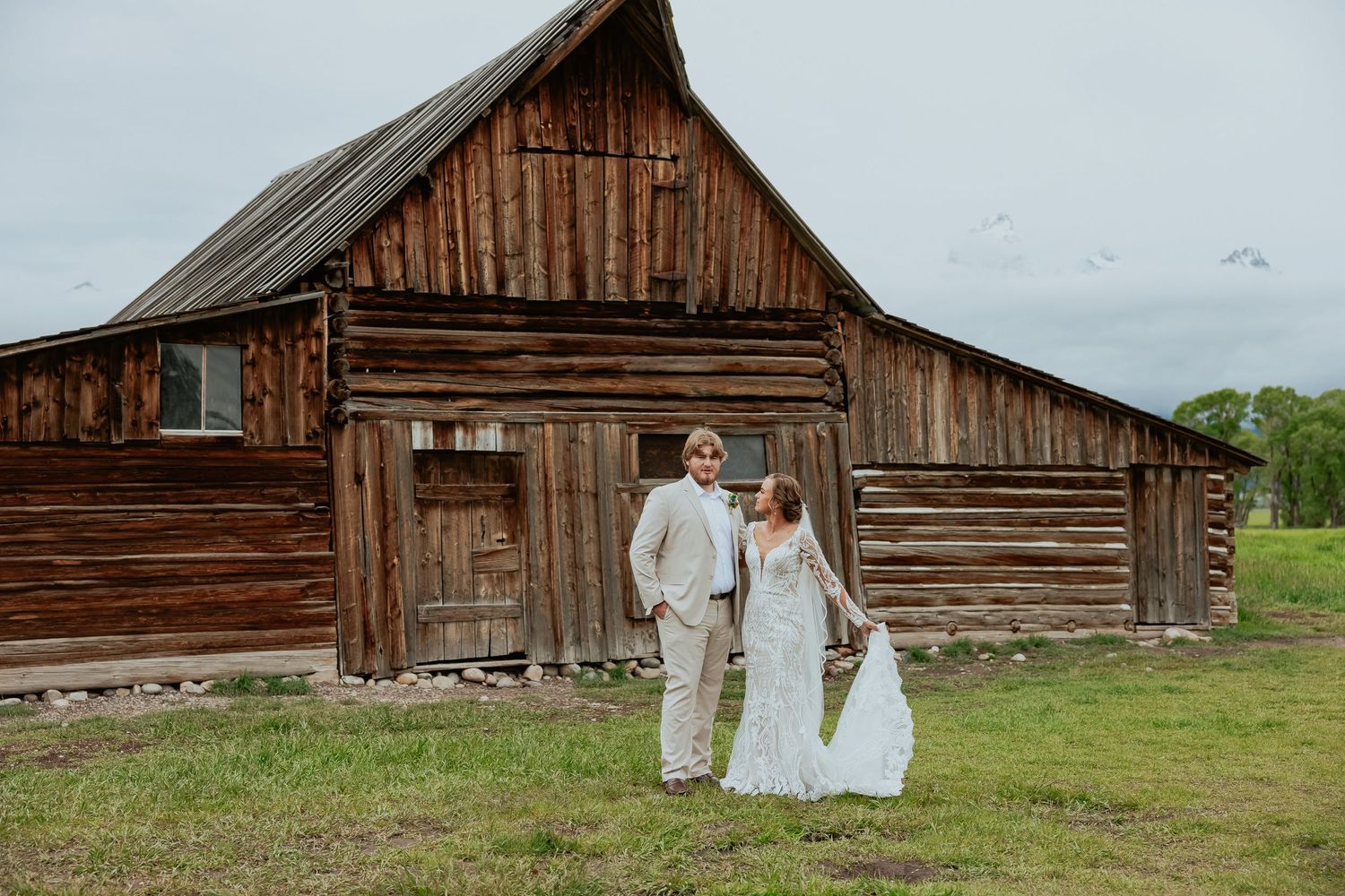 A rustic wedding photo in front of a weathered wooden barn.