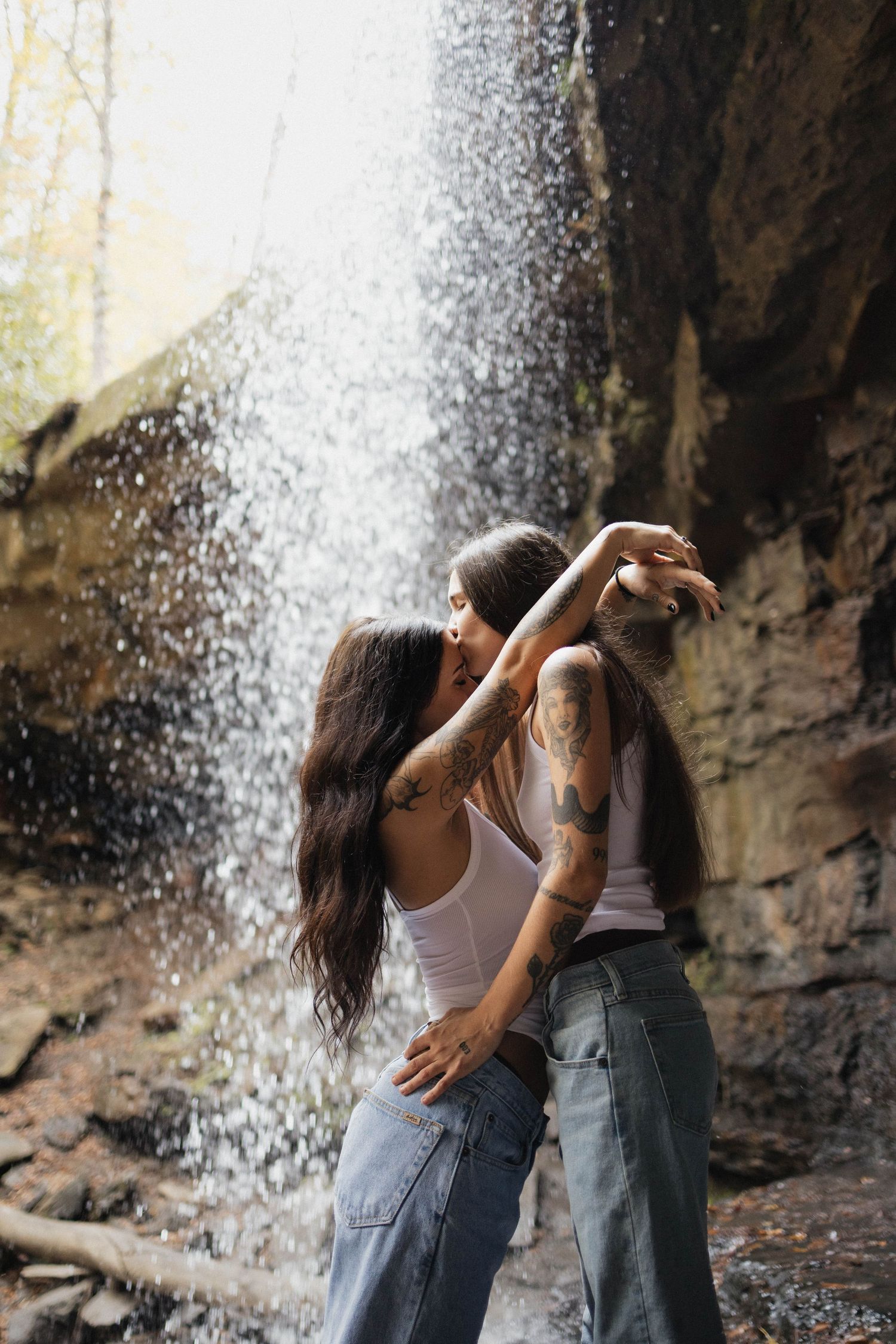 Two dancers perform an intimate contemporary dance sequence under a cascading waterfall in nature.