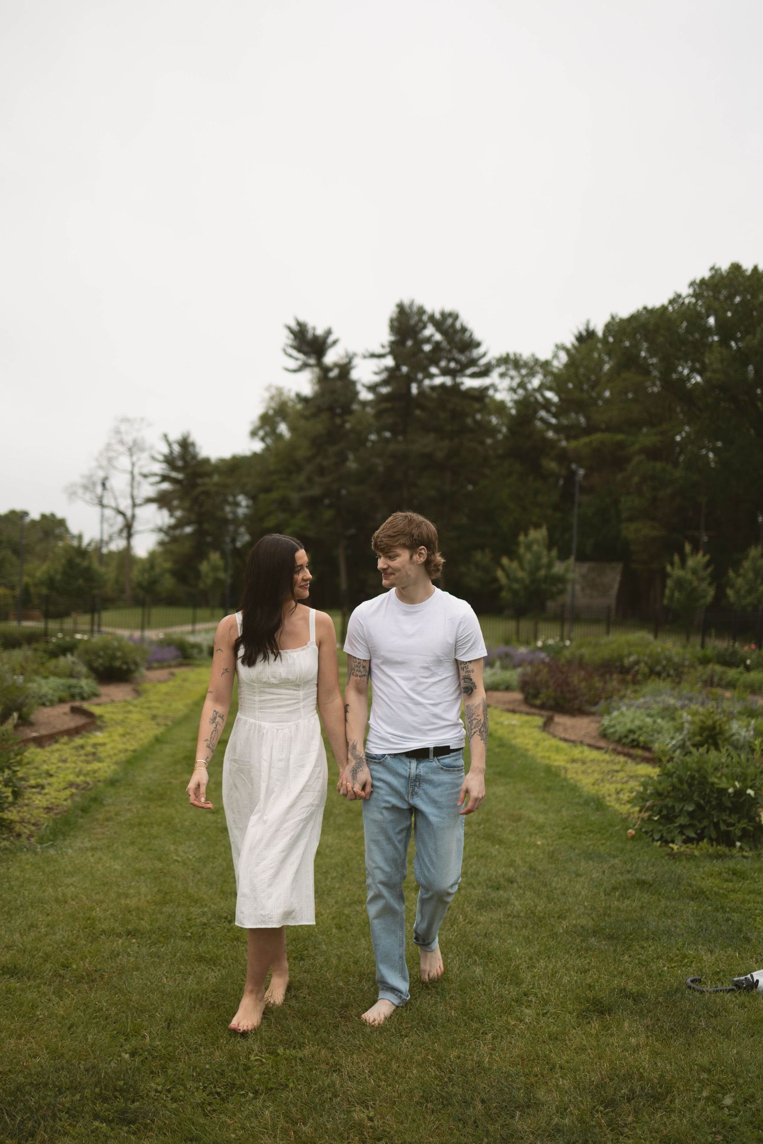 A couple walks hand in hand through a lush green garden path on a summer day.