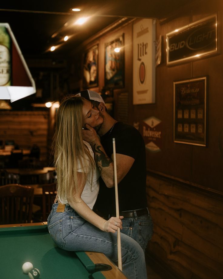 A couple shares an intimate moment at a dimly lit pool table in a bar setting.