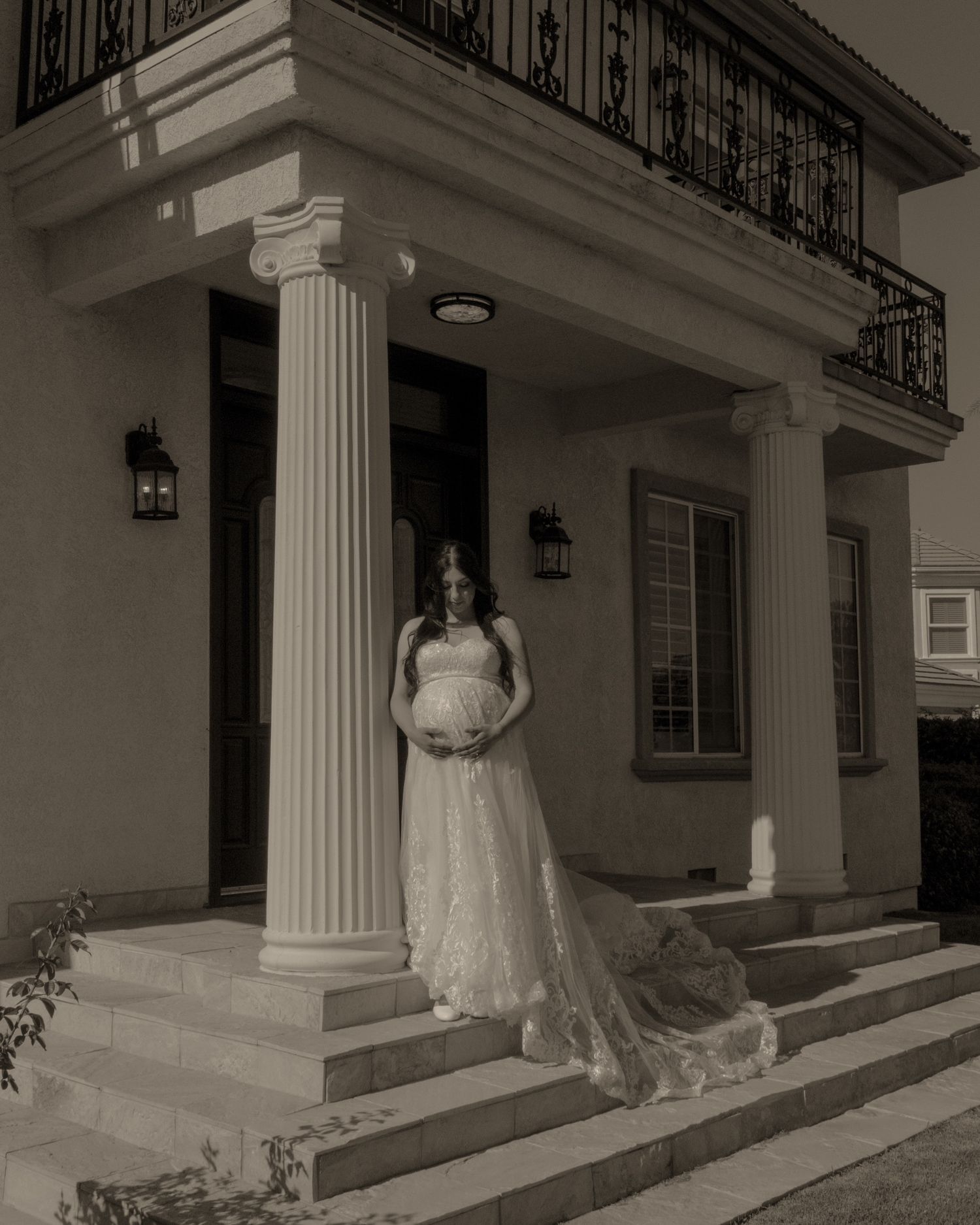 An elegant sepia photograph shows a bride in a flowing lace gown and veil standing on a grand porch with white columns.