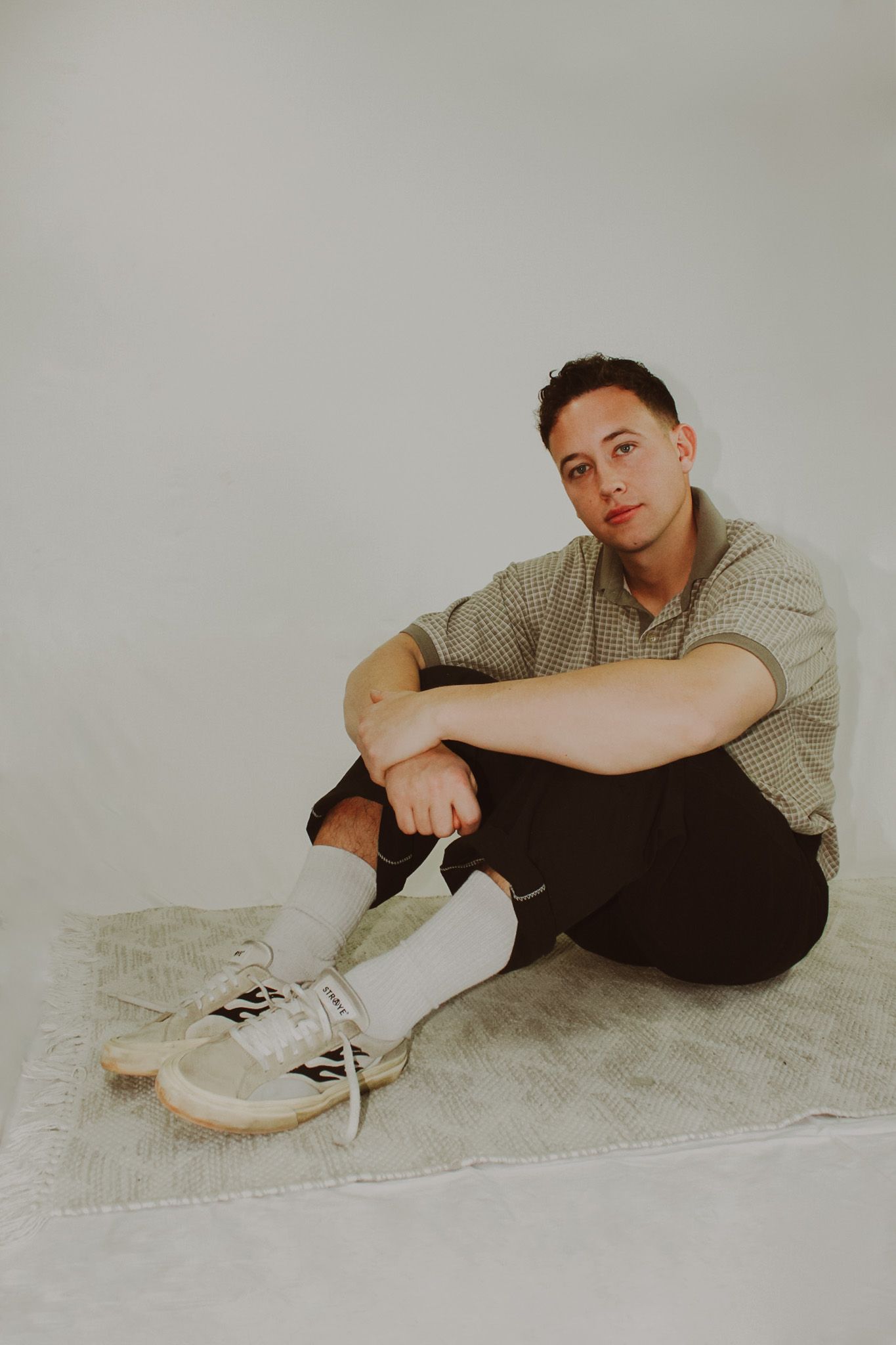 Casual portrait against grey background wearing knit sweater and classic sneakers.