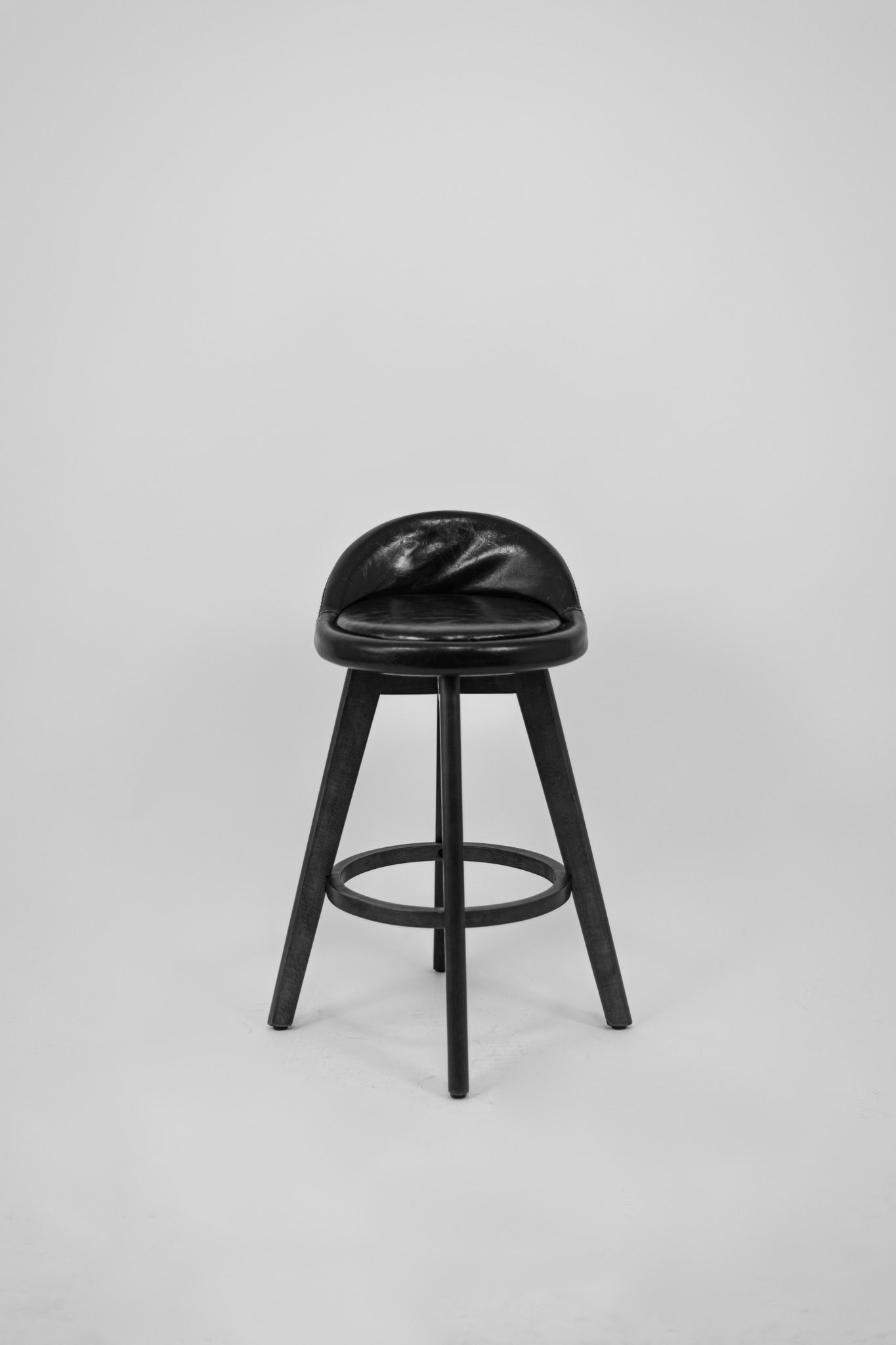 Minimalist black bar stool with cushioned seat photographed in monochrome style.