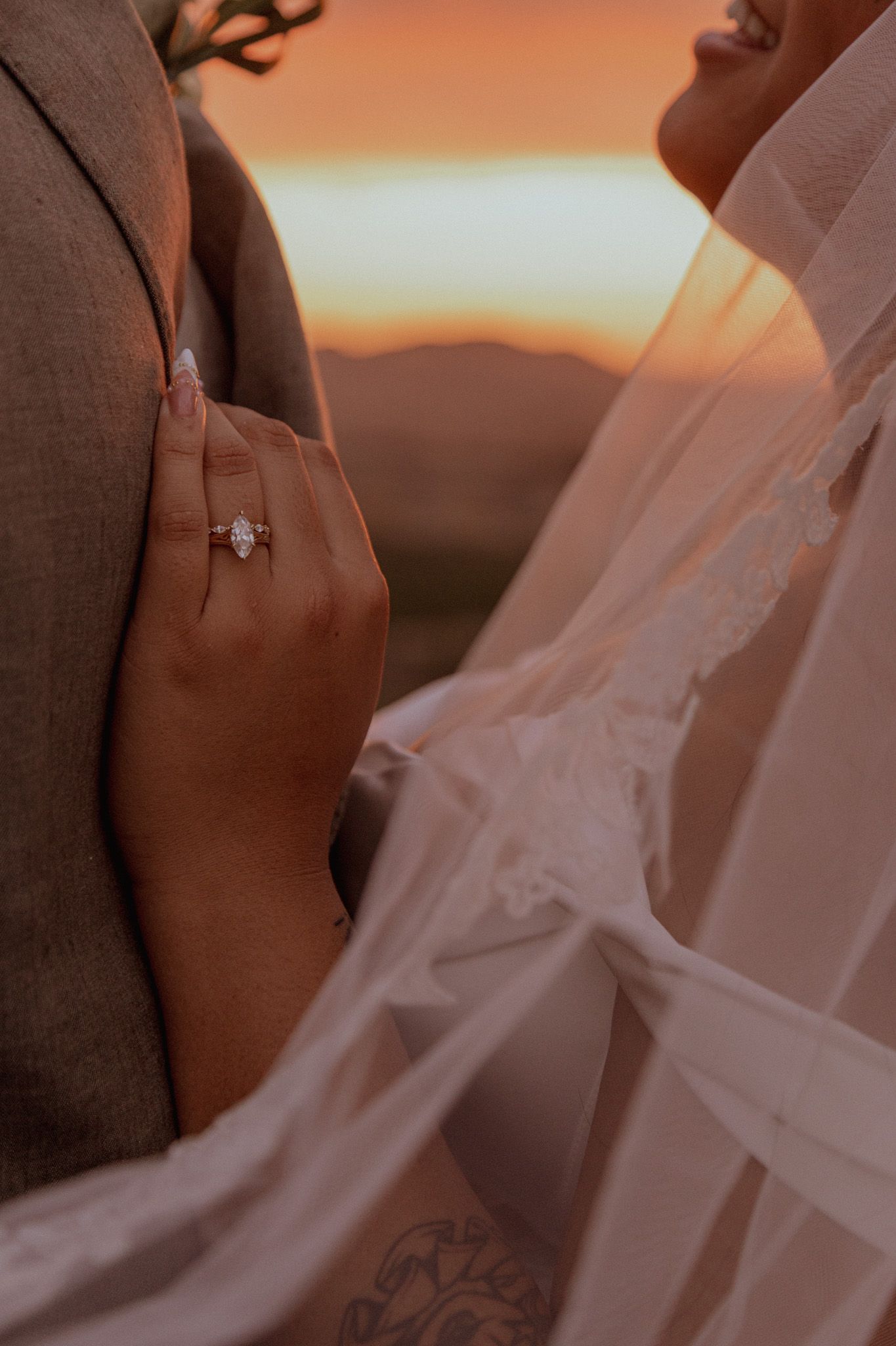 A close-up shot of hands displaying an engagement ring against a warm sunset sky background.