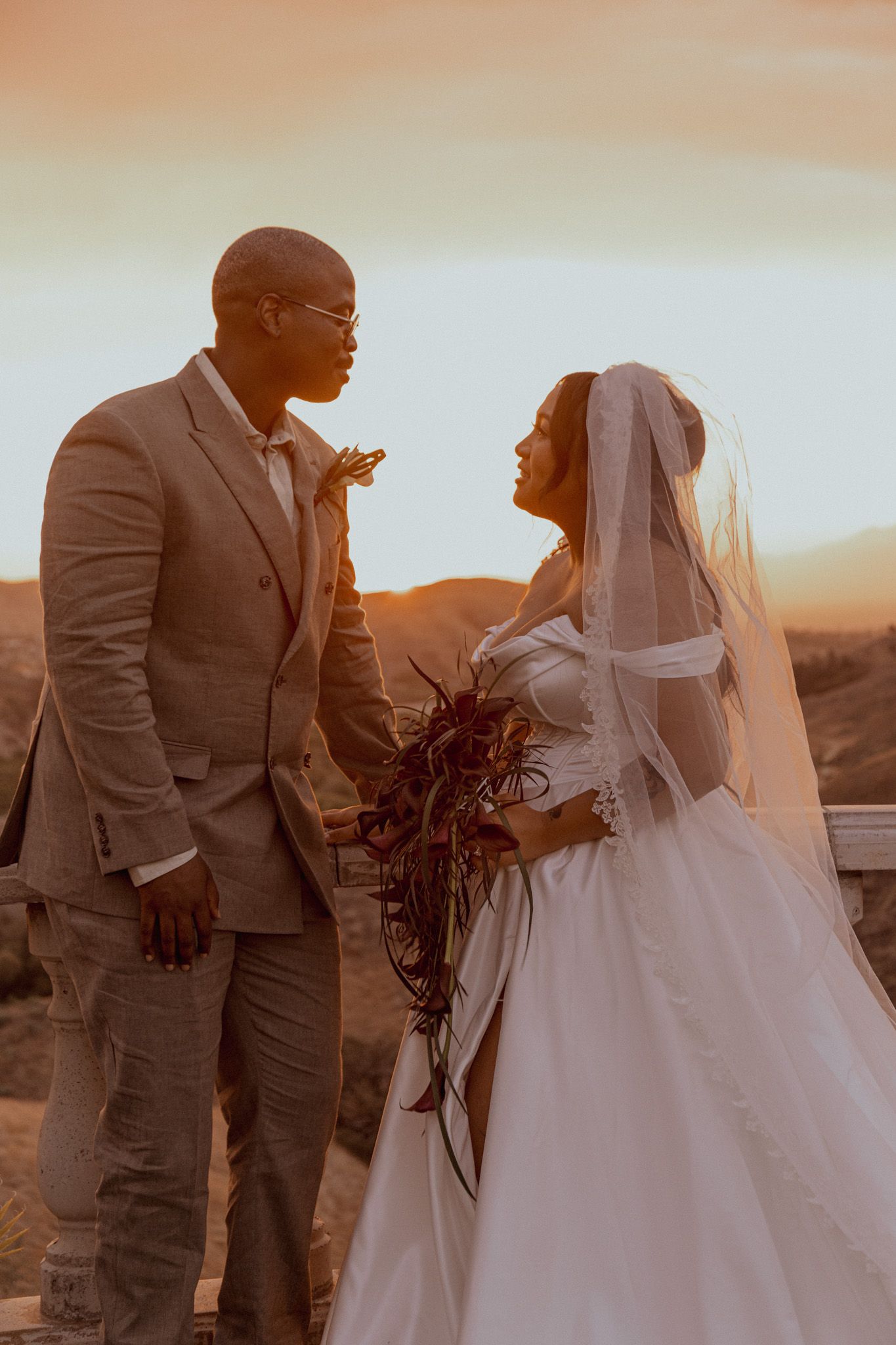 A bride and groom share an intimate moment at sunset during their desert wedding photoshoot.