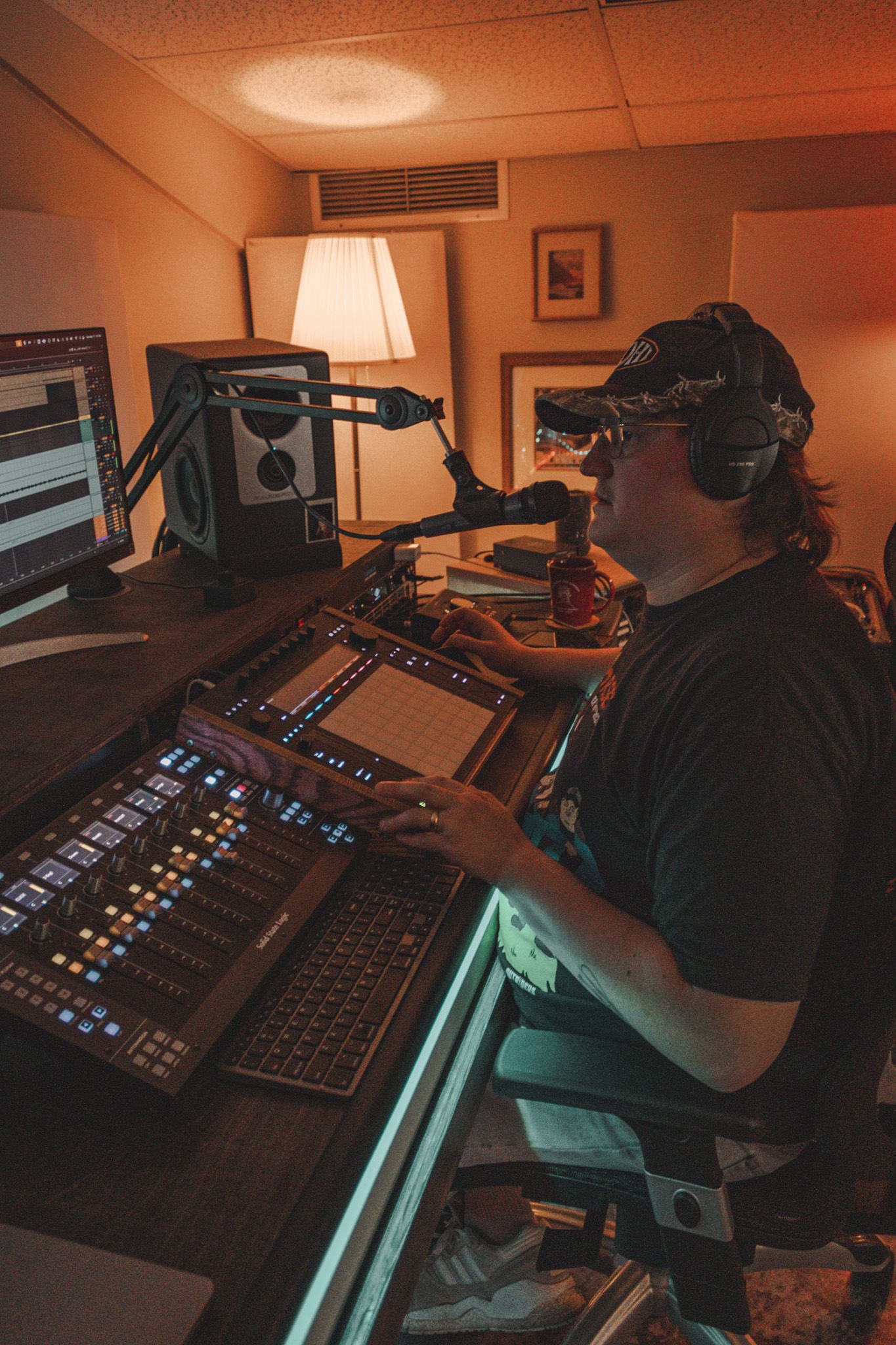 Audio engineer working at a professional mixing console with headphones in a dimly lit broadcast studio.