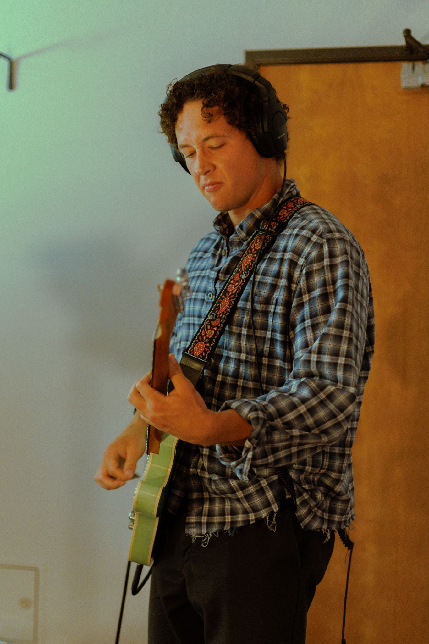 Musician in plaid button-down shirt plays electric guitar during performance in warm lighting.