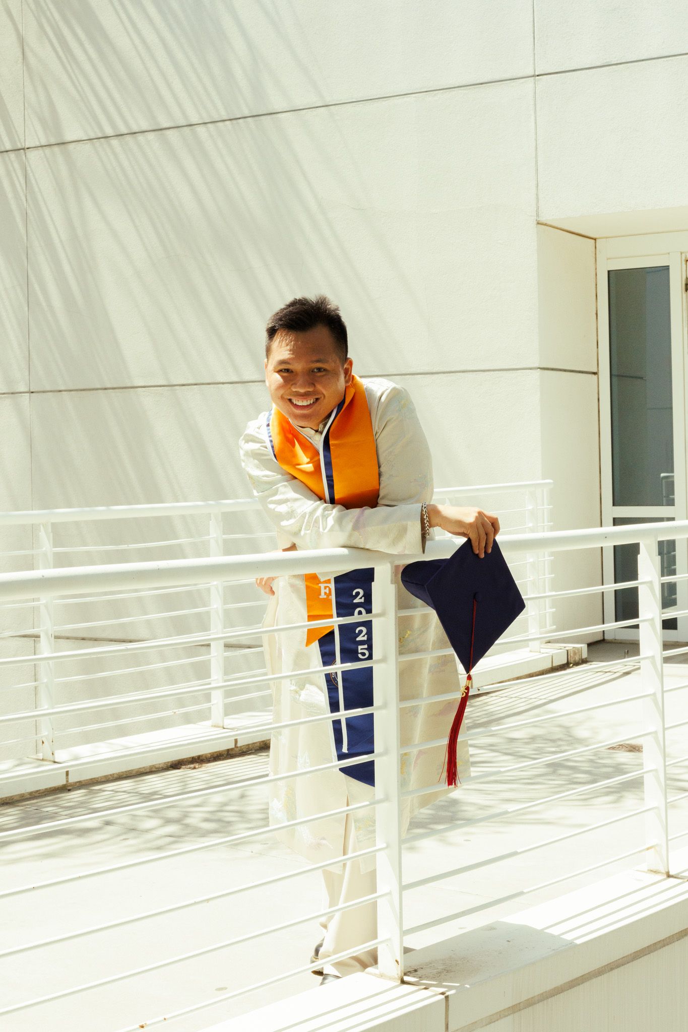 Athletic person in orange vest and white pants smiles while leaning on railing in modern building with natural light.