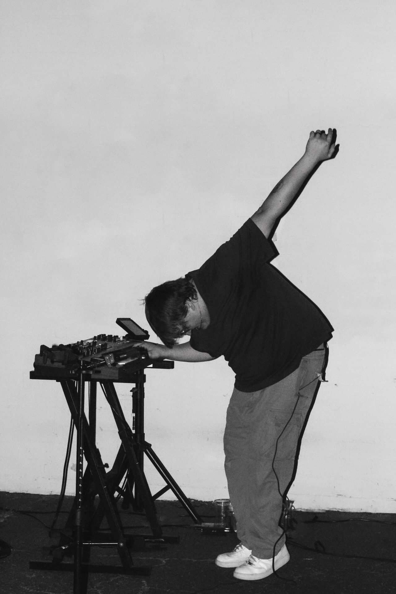 A DJ leans over electronic music equipment in a dynamic black and white performance shot.