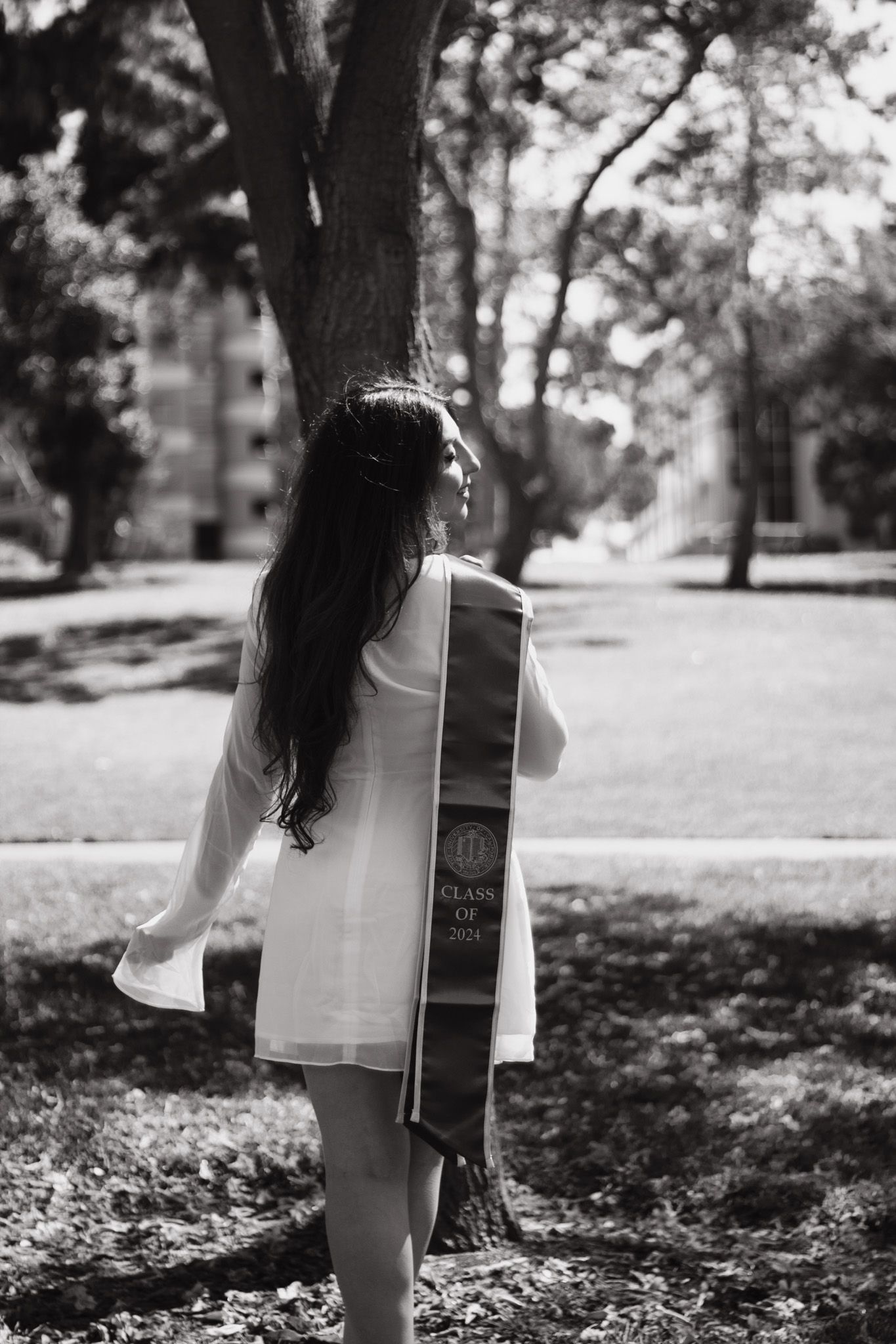 Black and white photo of someone holding large book near tree in park setting.