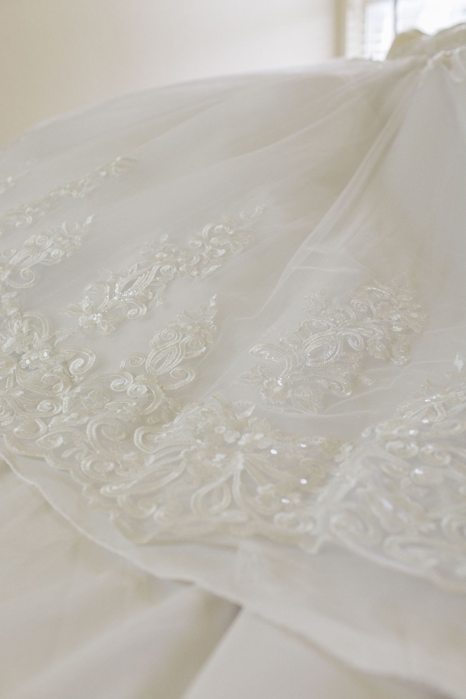 Close-up view of delicate white lace and sequin embellishments on a wedding dress fabric.