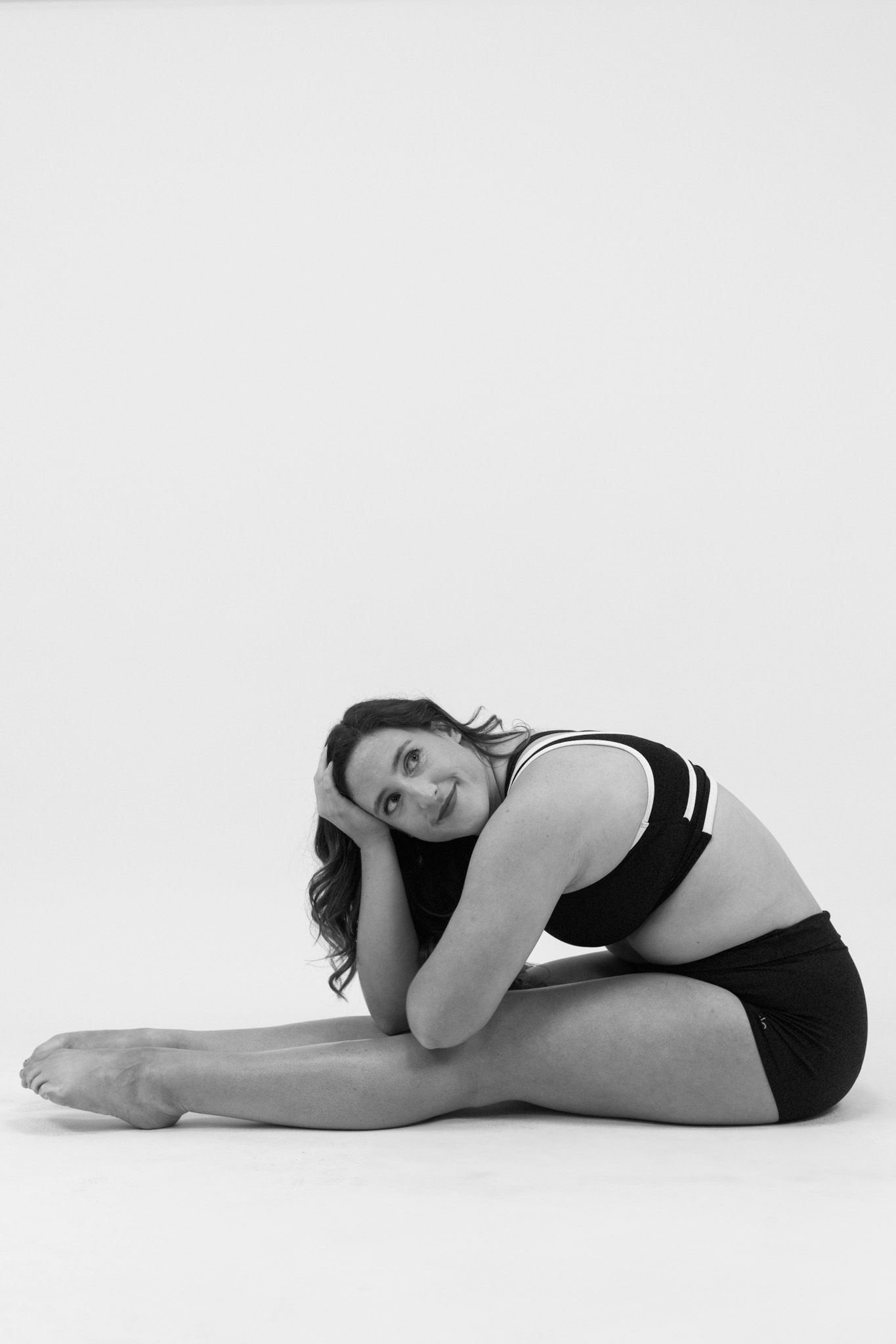 A figure in black athletic wear performs a seated forward bend stretch pose against a white background.