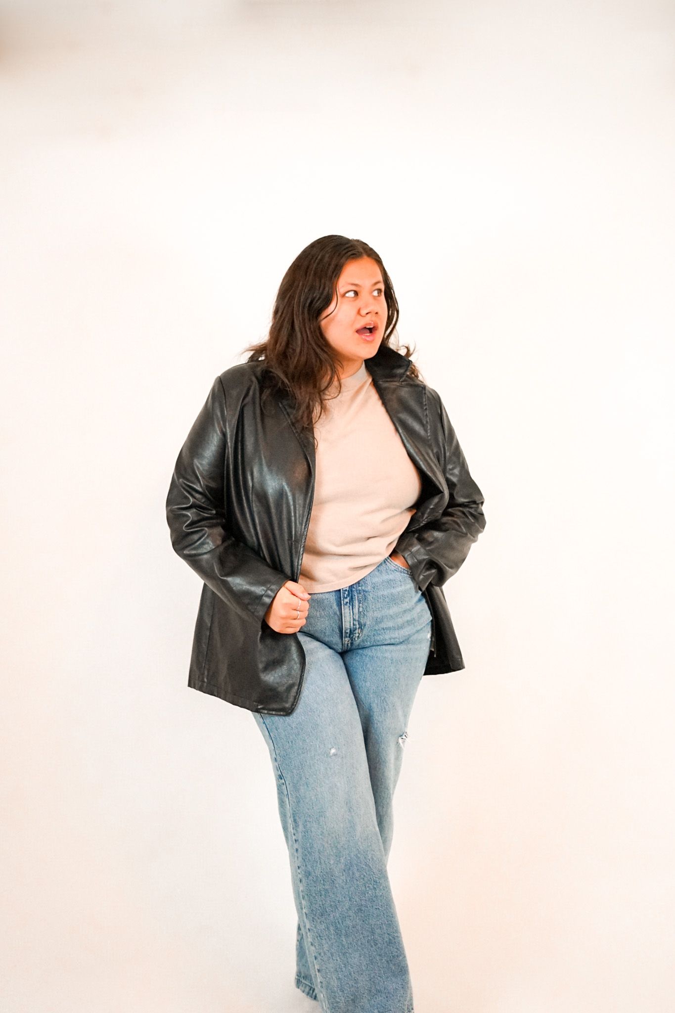 Fashionable outfit featuring a black leather jacket and wide-leg jeans captured in a bright studio setting.