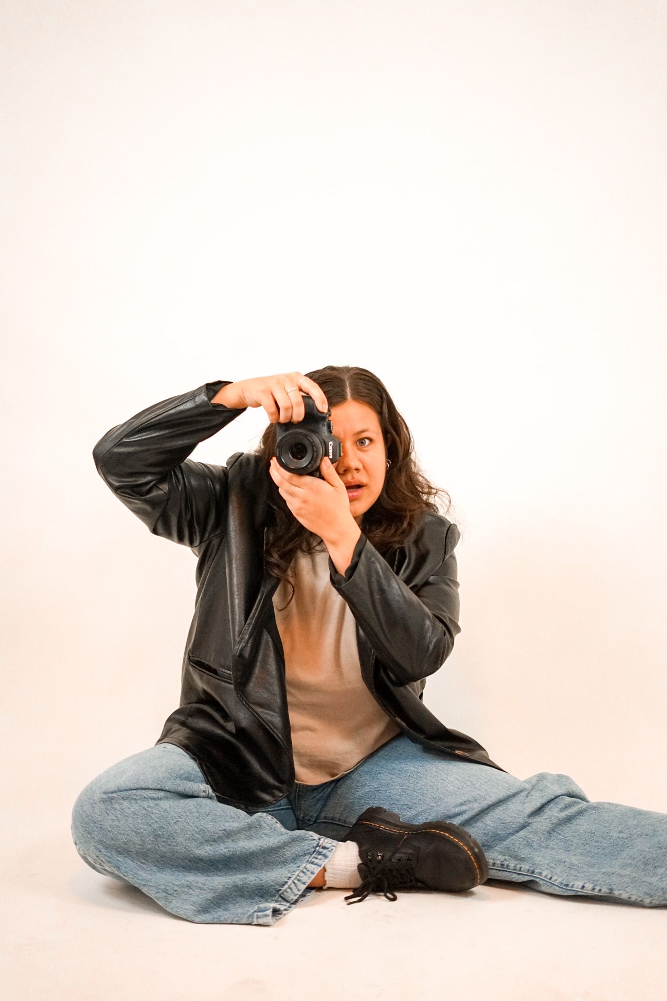 Photographer in casual outfit sitting cross-legged while taking a picture with professional camera.