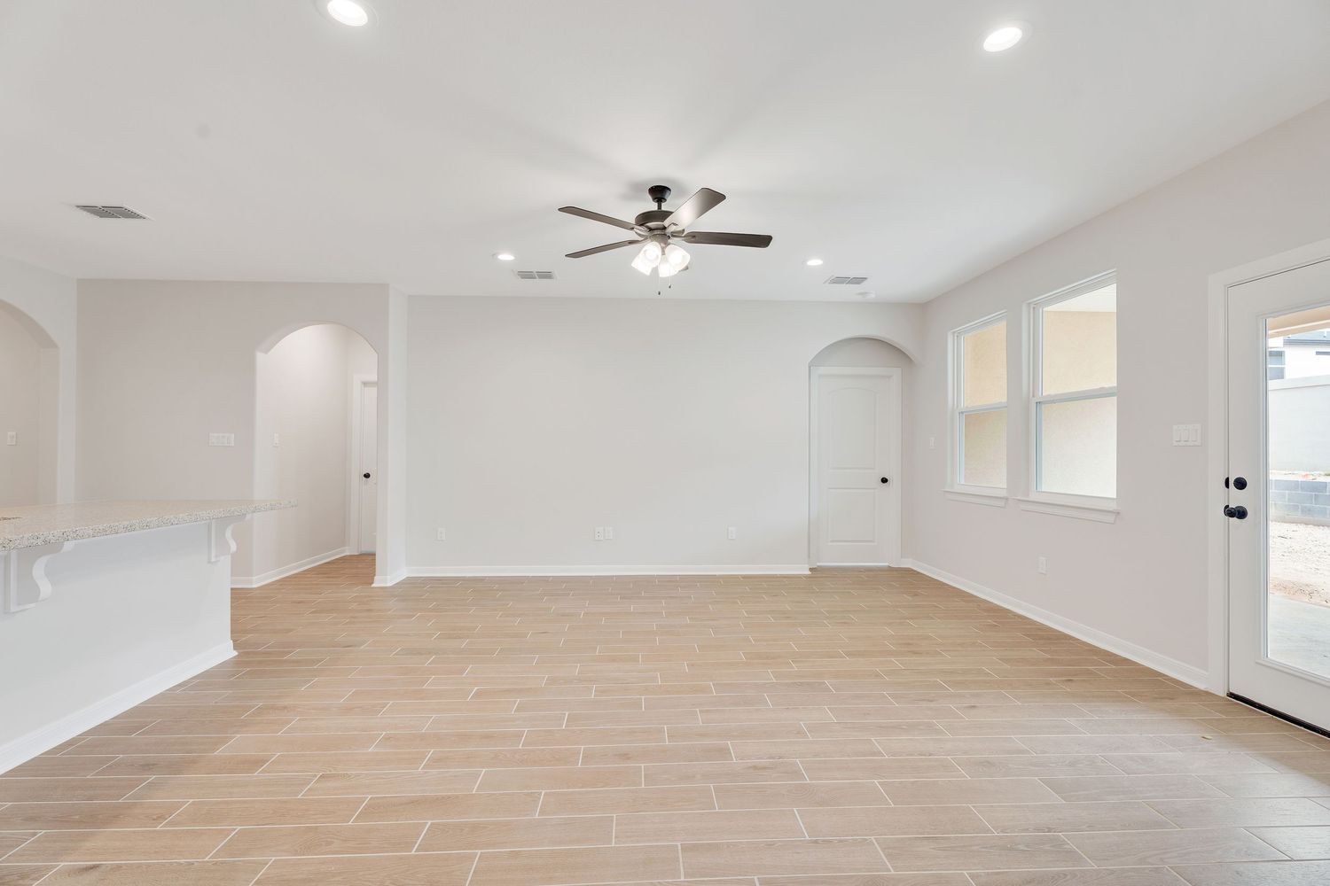 A bright, modern open concept living space with light hardwood floors and recessed lighting in a white ceiling.
