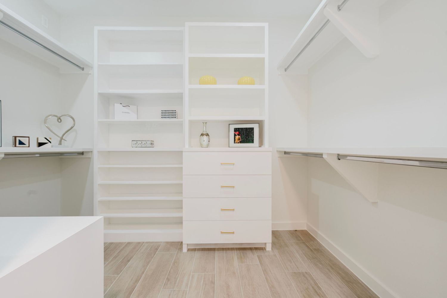 Custom white walk-in closet with built-in drawers, shelving, and light wood floors.