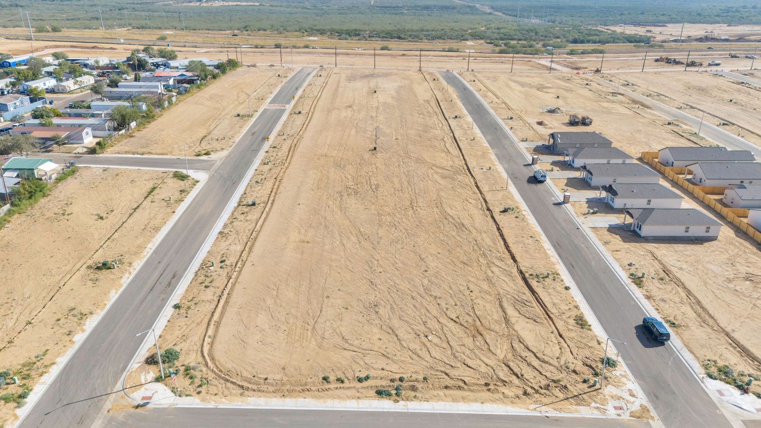Aerial panoramic view of a long empty highway stretching through desert terrain with scattered buildings in the distance.