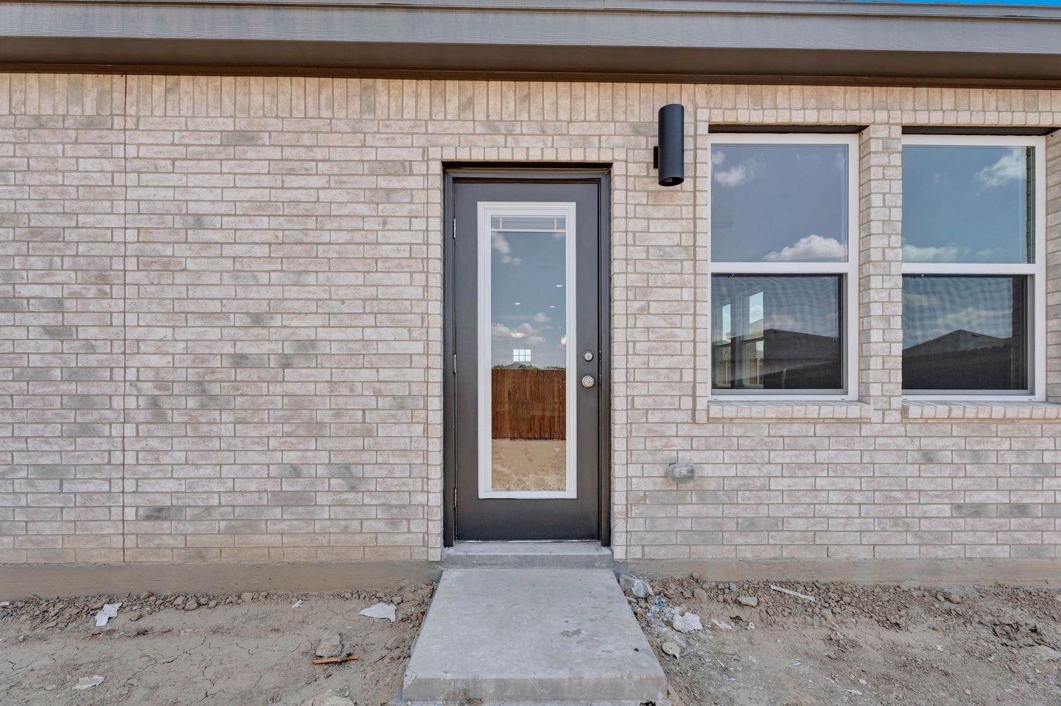 New construction brick home exterior featuring a dark-framed glass door and large window on a concrete step entryway.
