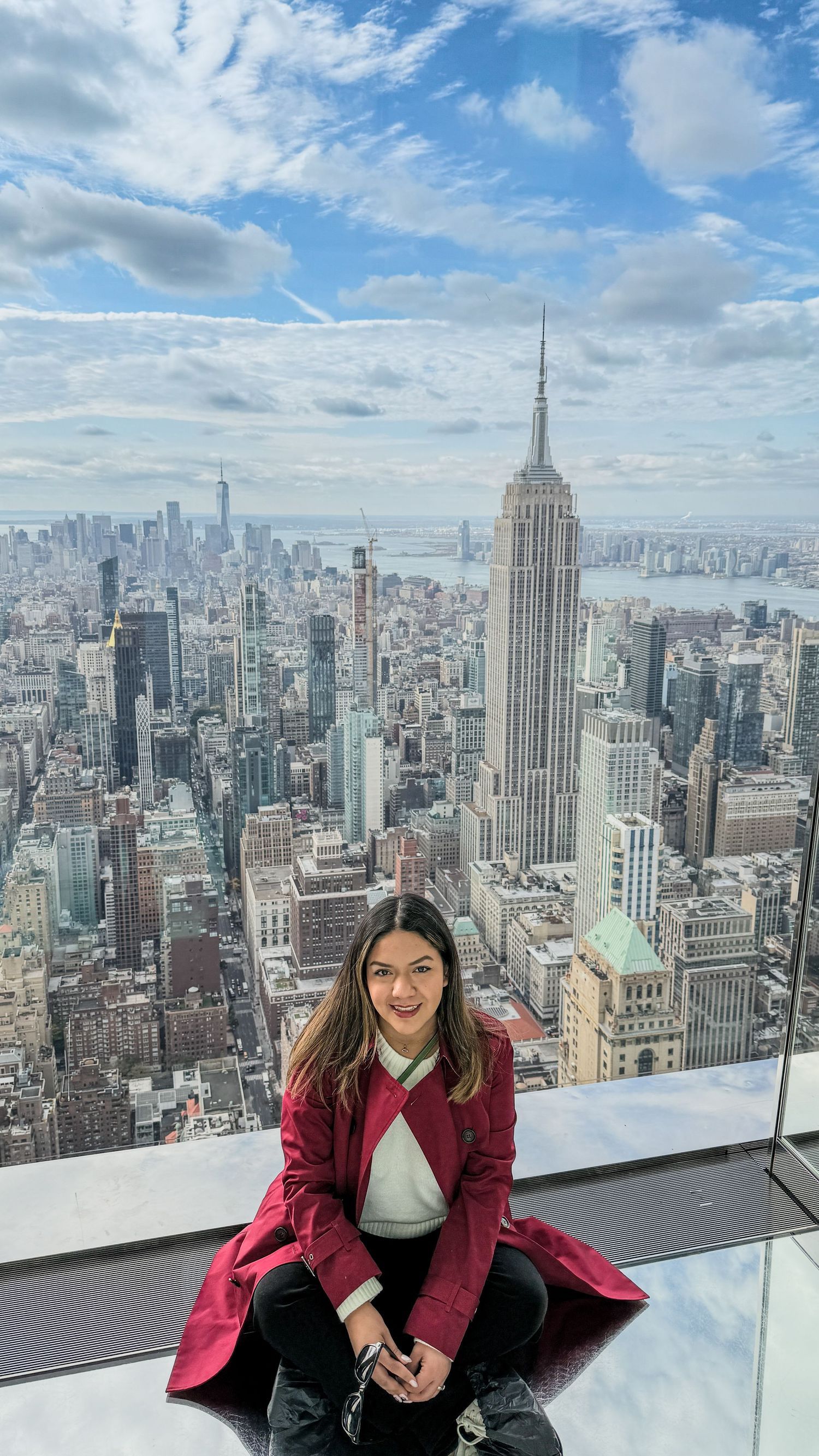 Panoramic view of Manhattan skyline featuring Empire State Building under cloudy blue sky.
