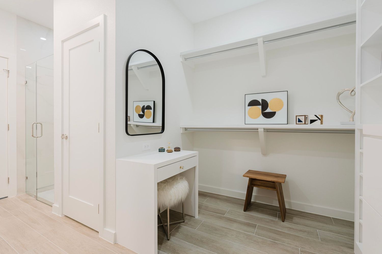Modern dressing area with arched mirror, white vanity table, and contemporary wall art.
