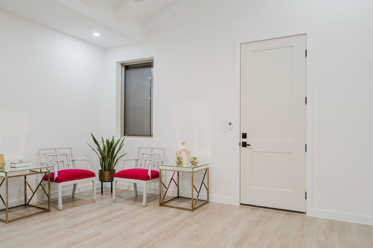 Elegant waiting area with gold accent tables, red cushioned chairs, and a potted plant beside white door.
