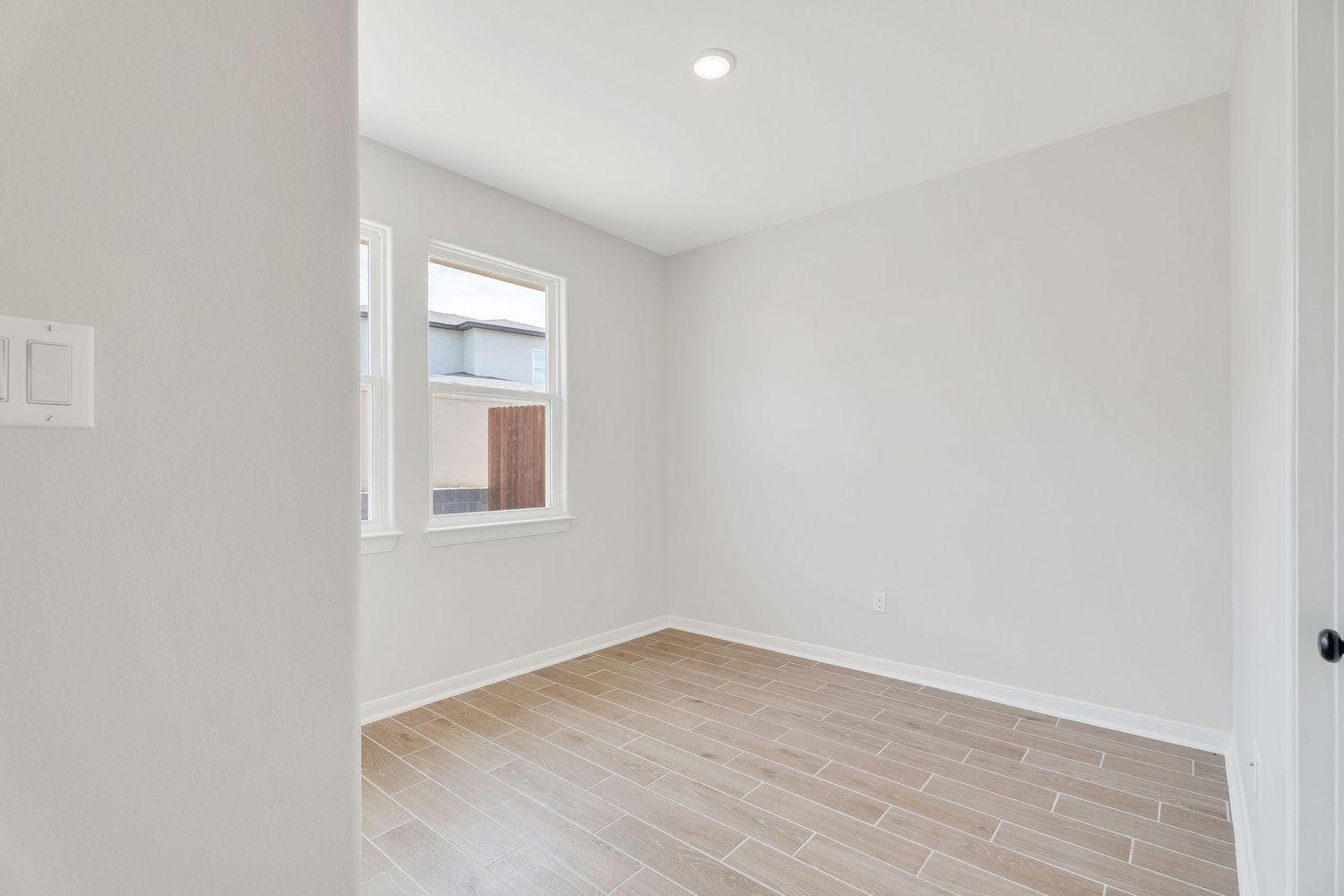 Modern empty room interior with white walls, light wood flooring, and natural light coming through windows.