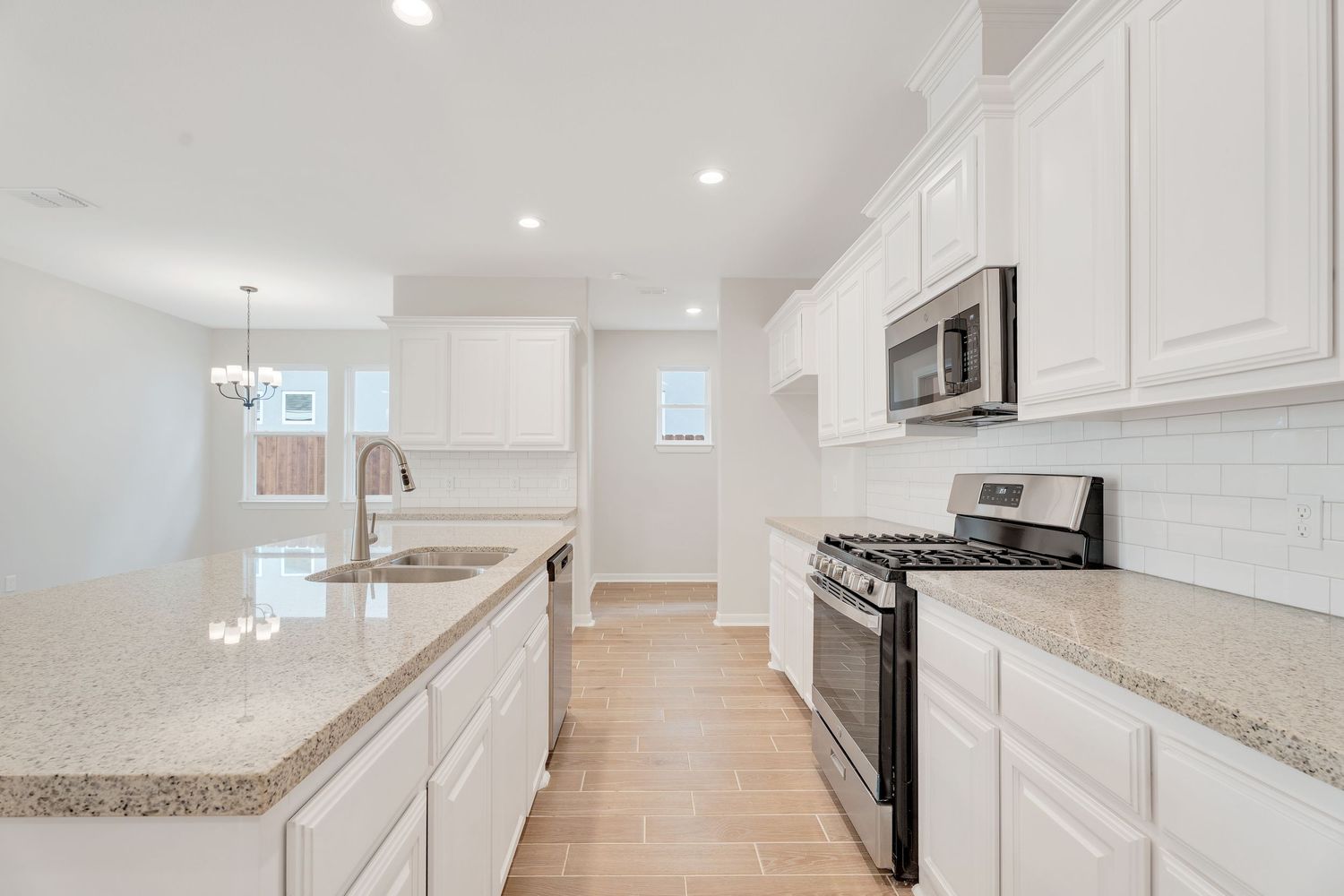 Modern white kitchen with granite countertops, stainless steel appliances, and recessed lighting in open concept layout.