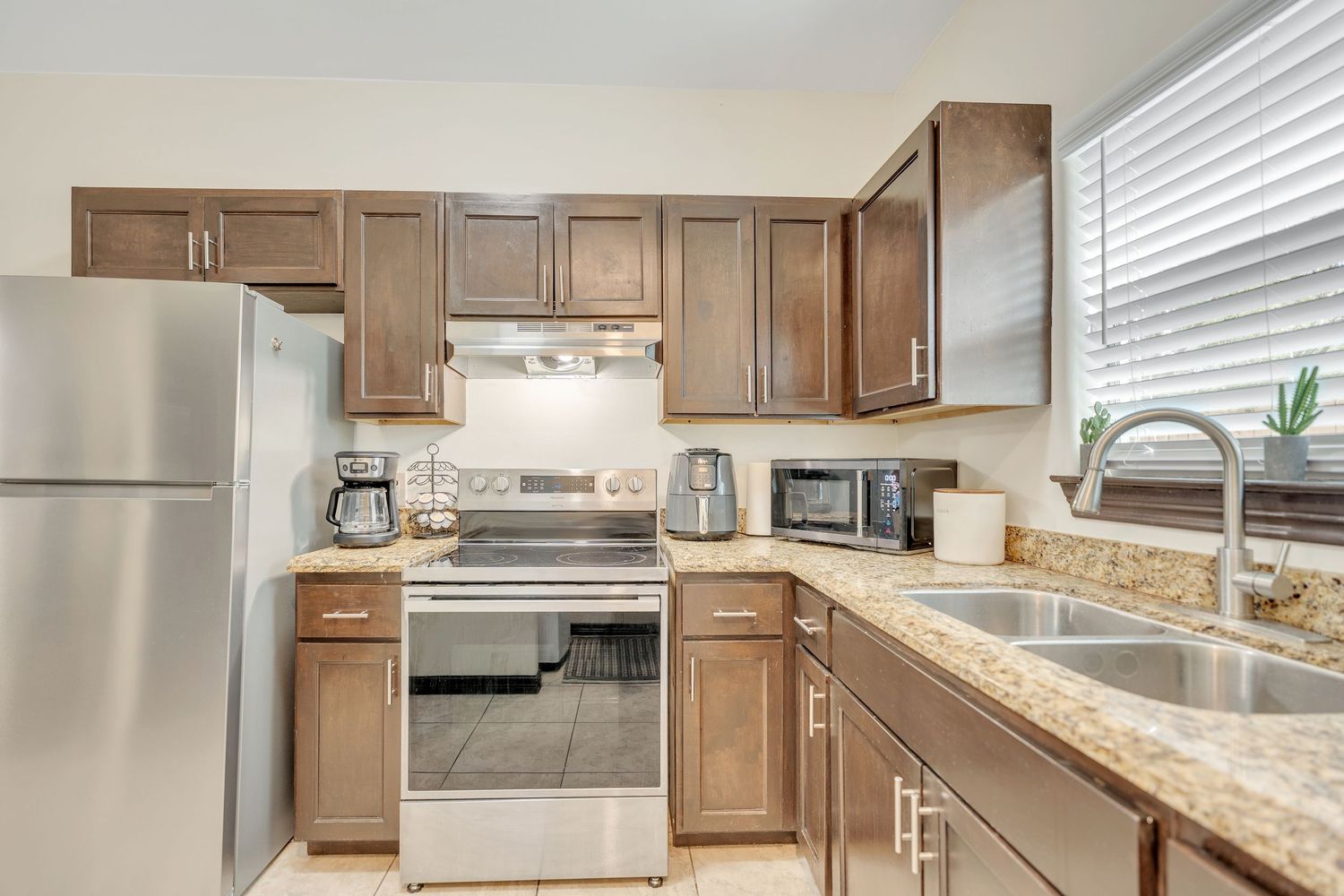 Modern kitchen features brown cabinets, granite countertops, and stainless steel appliances in an open layout design.