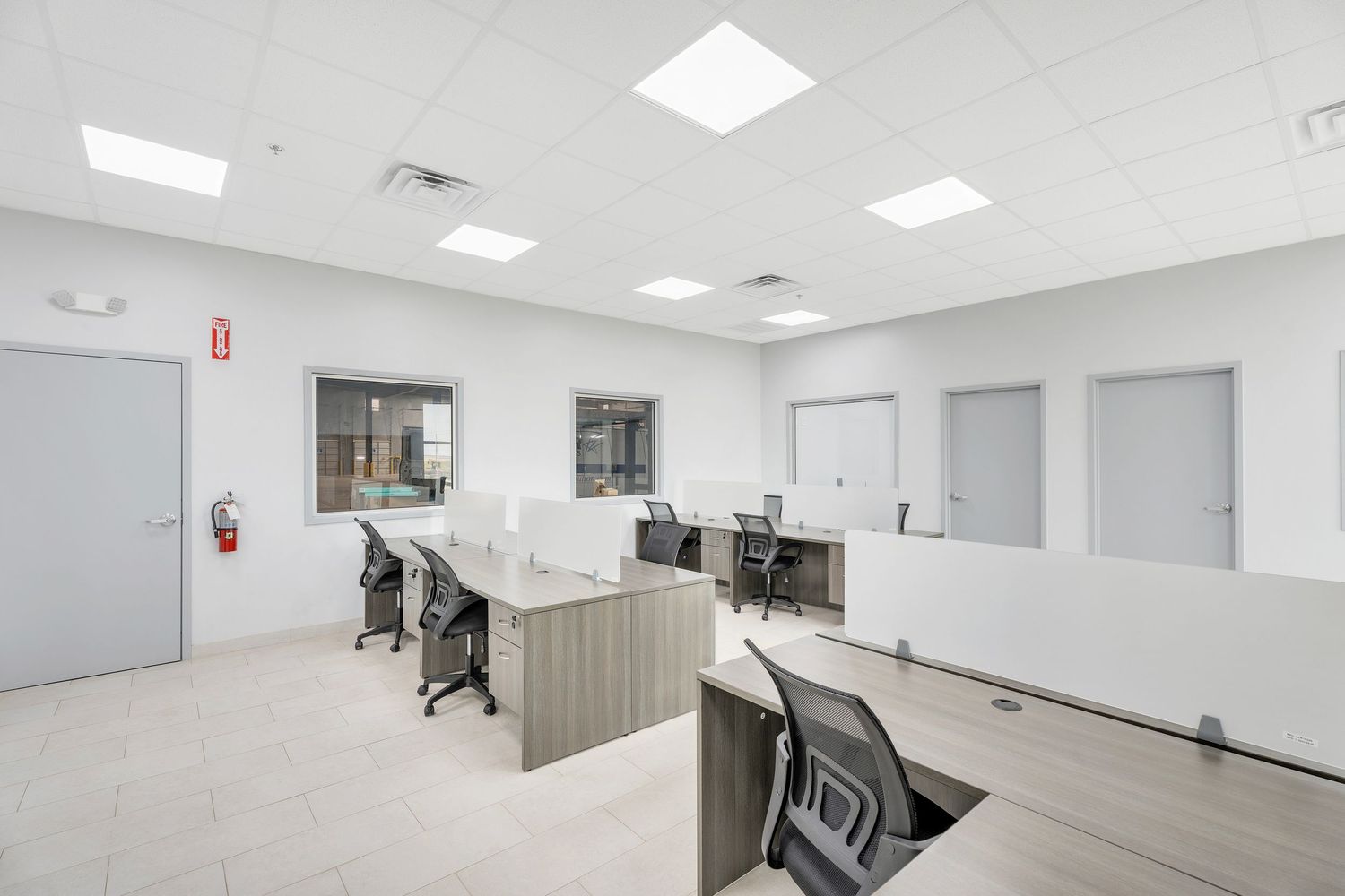 Modern office space with white walls, recessed lighting, and sleek workstations arranged in an open floor plan layout.