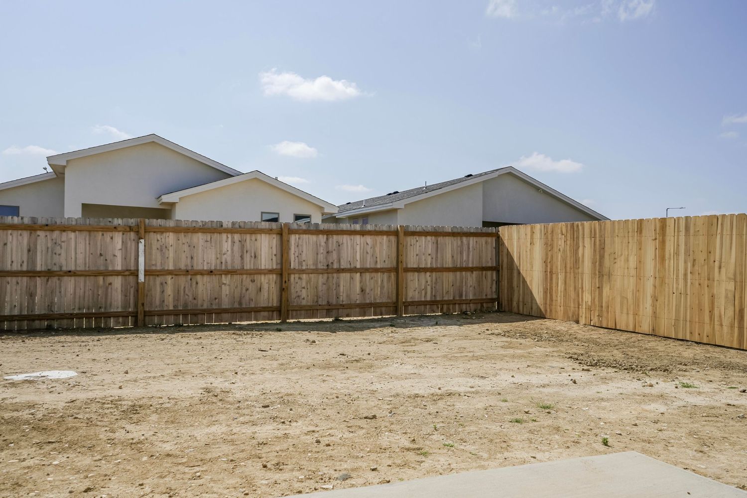 Wooden privacy fence surrounding an empty dirt backyard of residential homes.