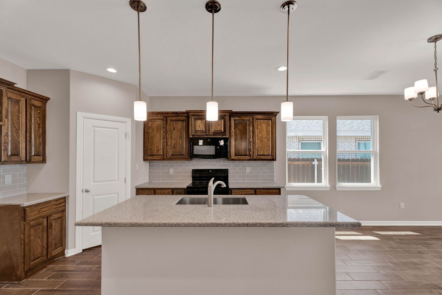 Modern kitchen with dark wood cabinets, granite island, pendant lights, and subway tile backsplash.