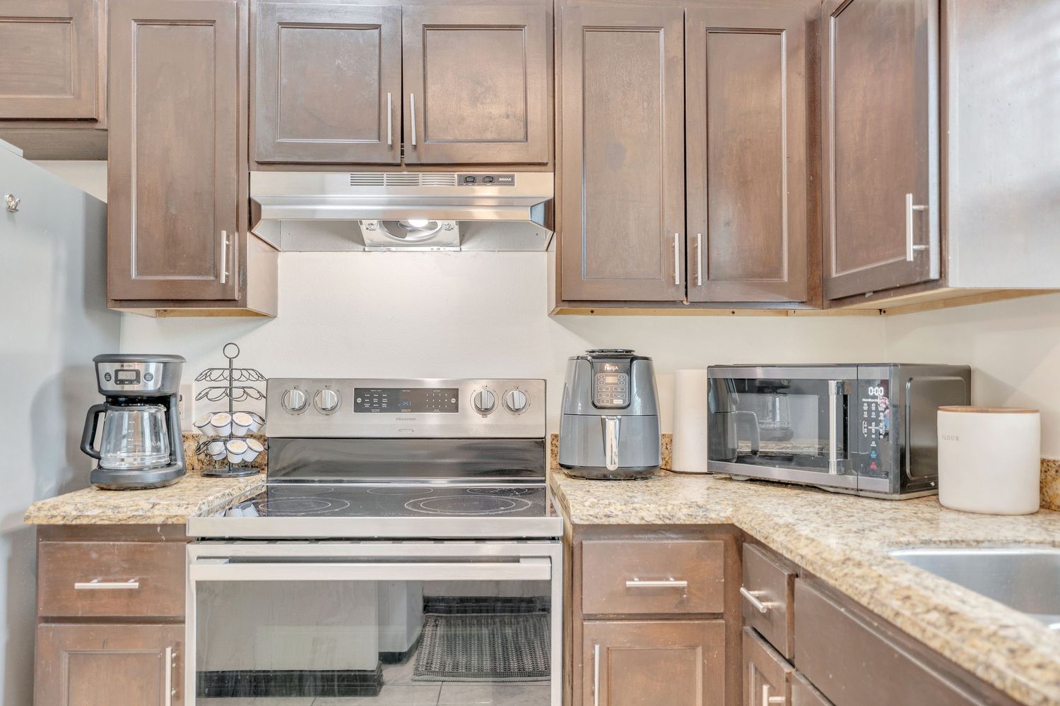 Modern kitchen interior with brown cabinets, stainless steel appliances, and granite countertops in neutral tones.