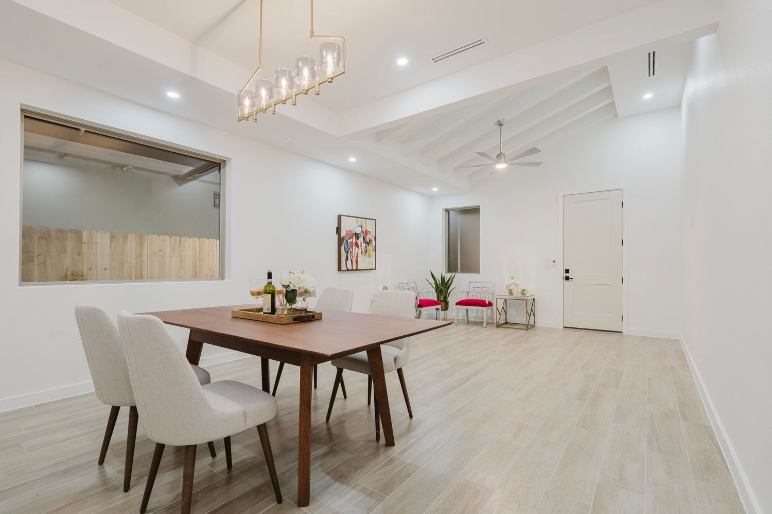 Spacious dining room with modern pendant lighting, wooden table, and upholstered chairs in white tones.