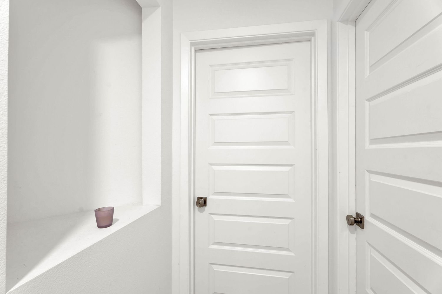 Clean white hallway with two panel doors, decorative niche, and purple accent piece.