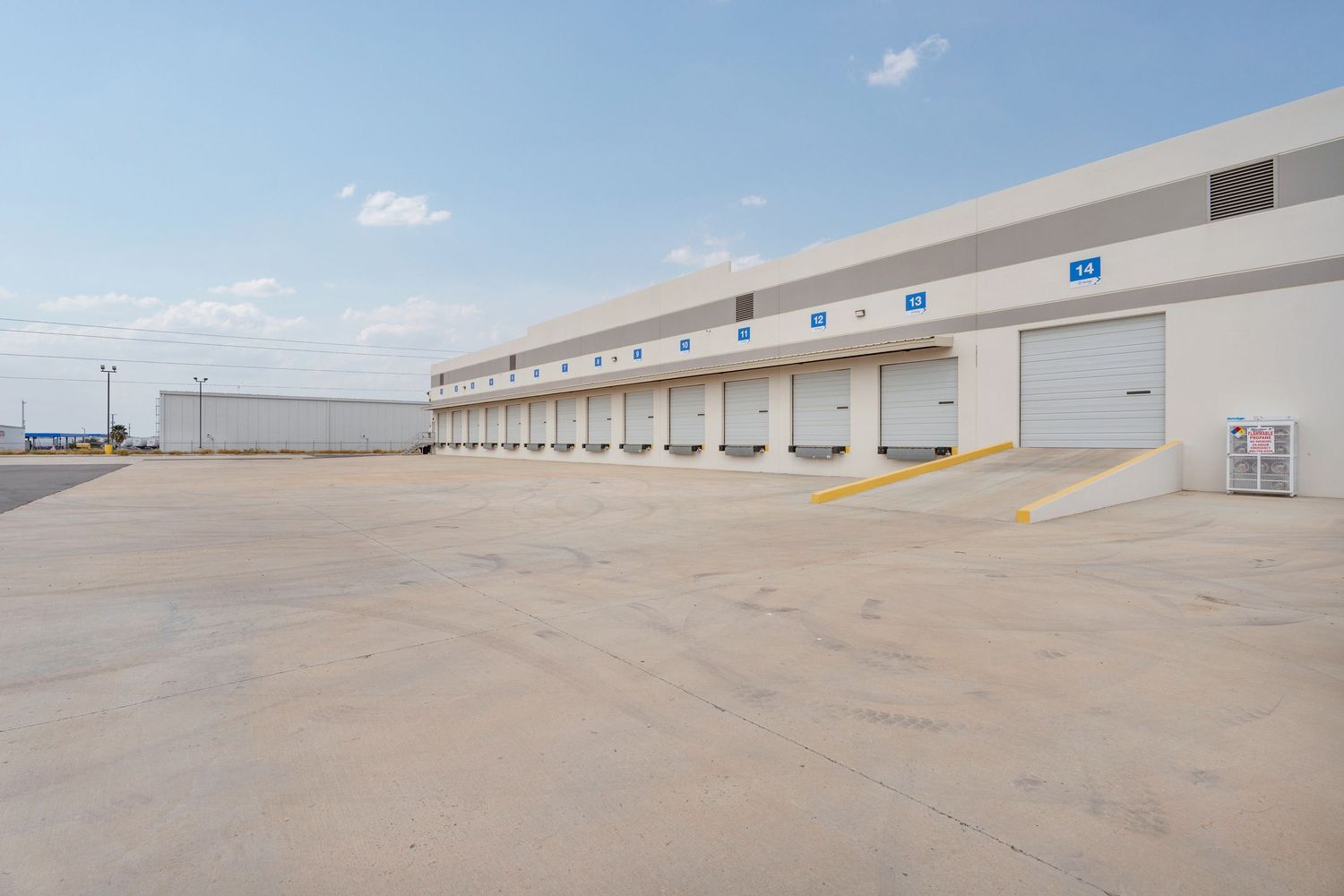 Loading dock doors line up along a commercial warehouse building exterior with a large empty concrete lot.
