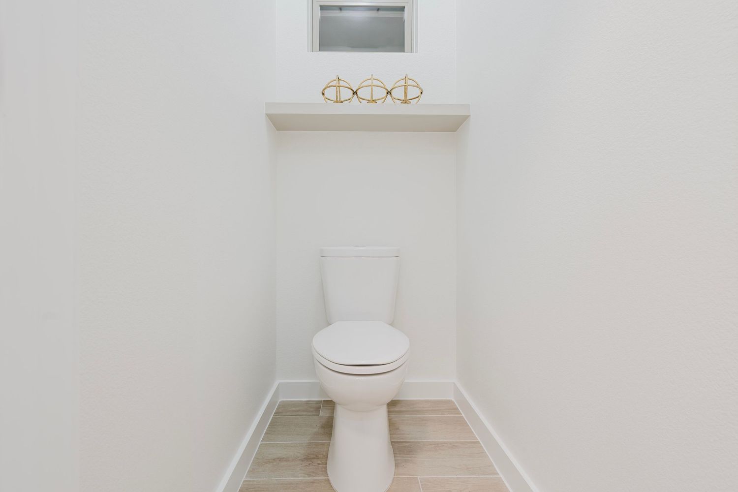 Clean white bathroom with toilet, light wood flooring, and modern vanity lighting.