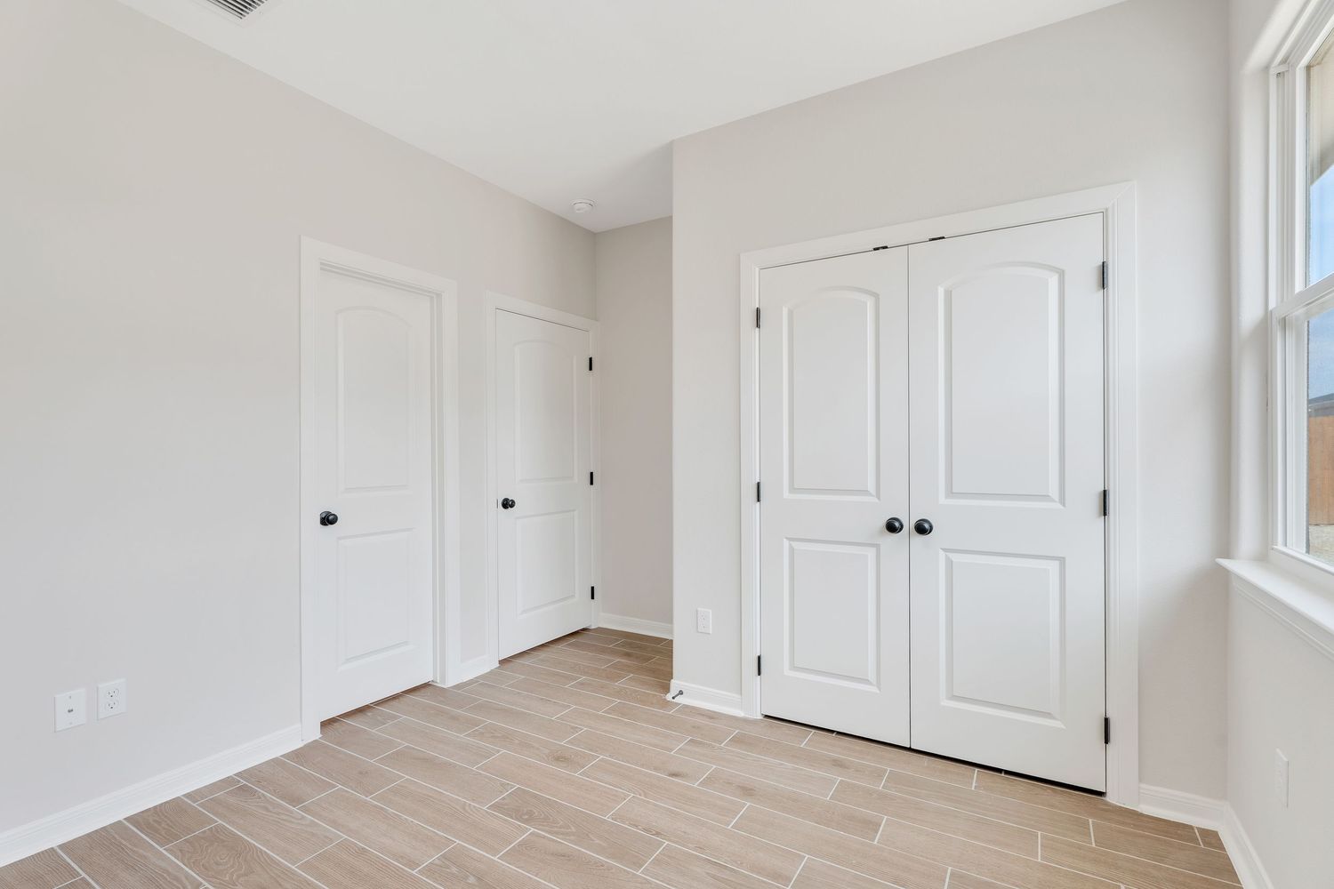 White interior room with hardwood floors, built-in cabinets, and natural light streaming through windows.