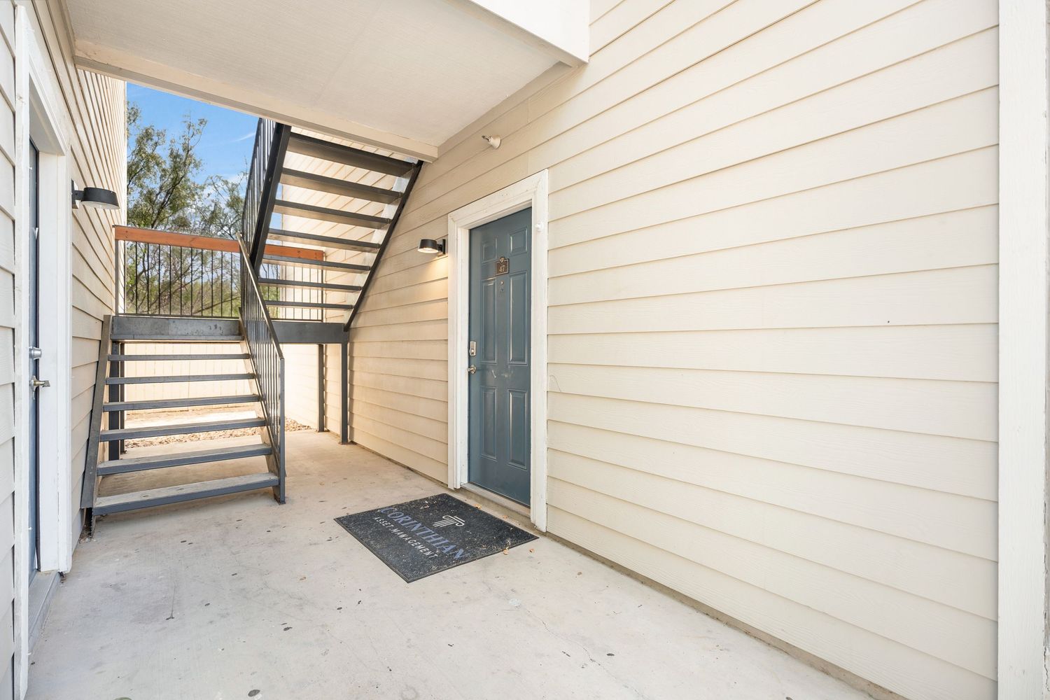 Exterior walkway and stairs along beige siding of residential apartment building with covered entryways.
